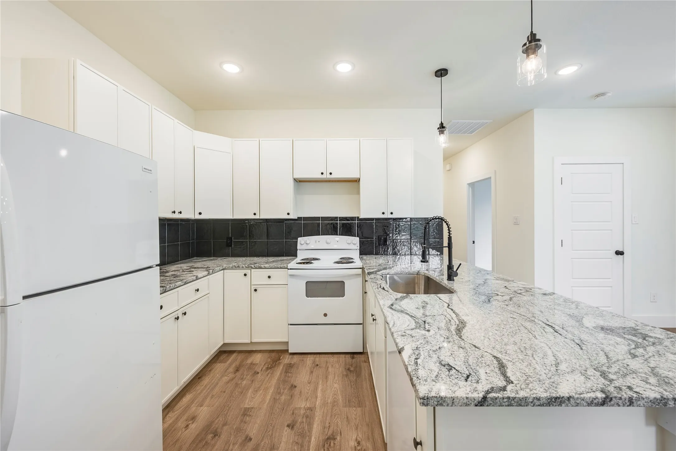 Kitchen featuring white cabinetry, a dark tile backsplash, a stainless steel sink with a black gooseneck faucet, and light-toned countertops