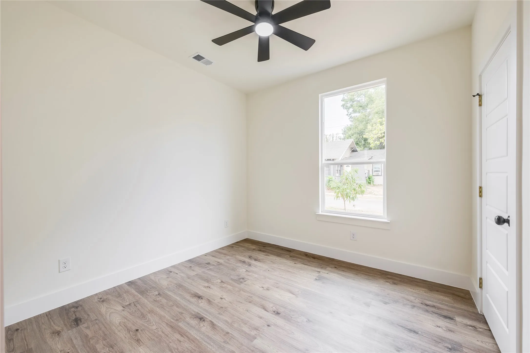 Wood-finish flooring, neutral wall tones, single window, white trim, and a ceiling fan