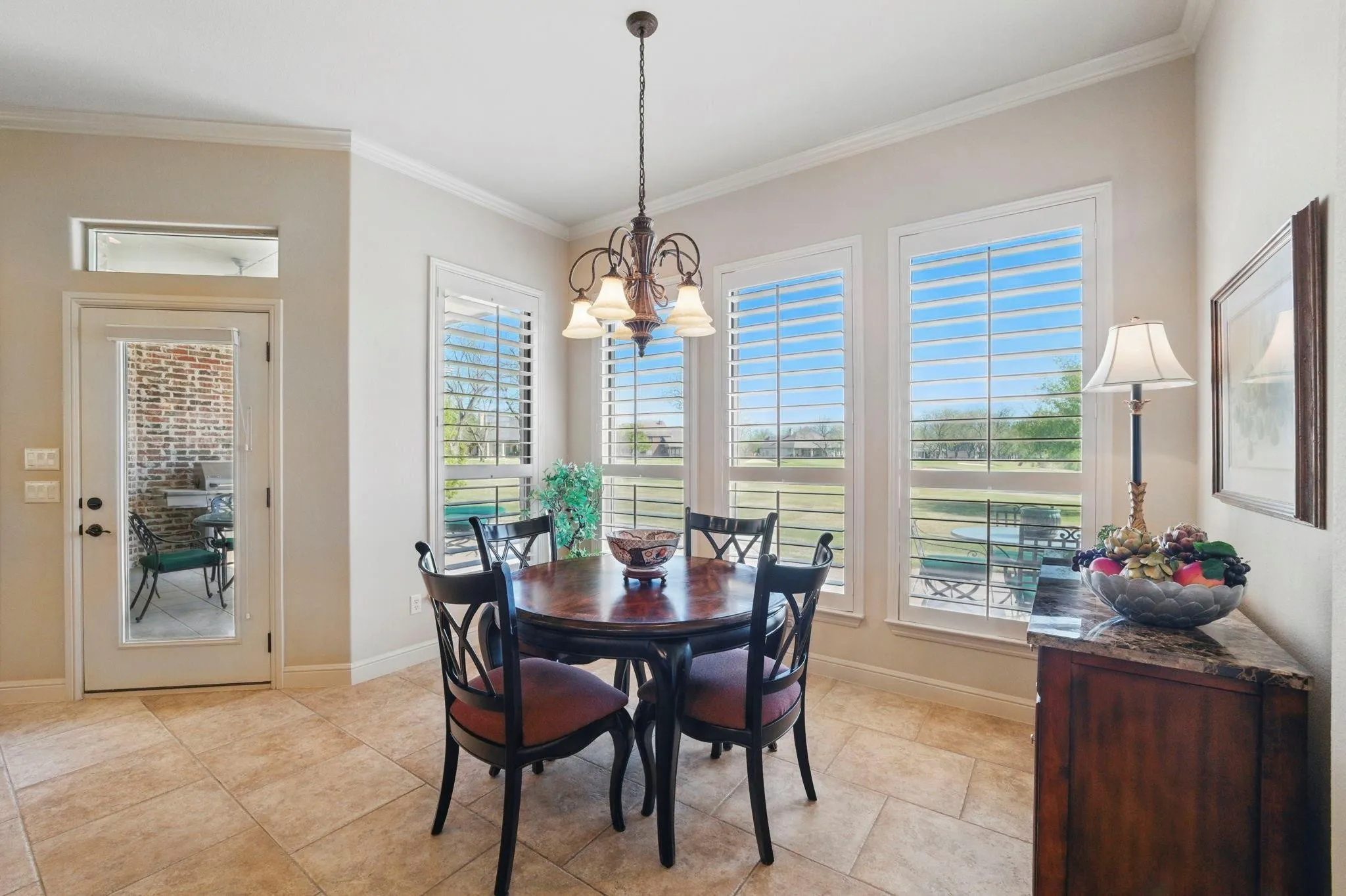 Travertine-style tile flooring, elegant crown molding, multiple windows with plantation shutters, a glass-paned door, and a built-in sideboard with a stone countertop