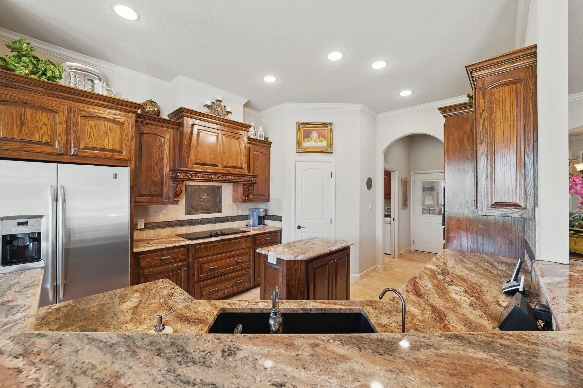 Kitchen featuring extensive cabinetry, stone countertops, a central island with sink, stainless steel refrigerator, and recessed lighting