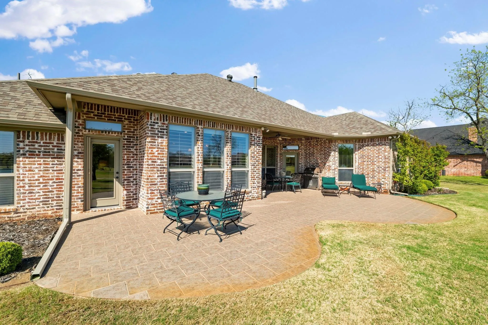 Expansive brick exterior with multiple large windows, a covered patio area, and an extensive stamped concrete patio