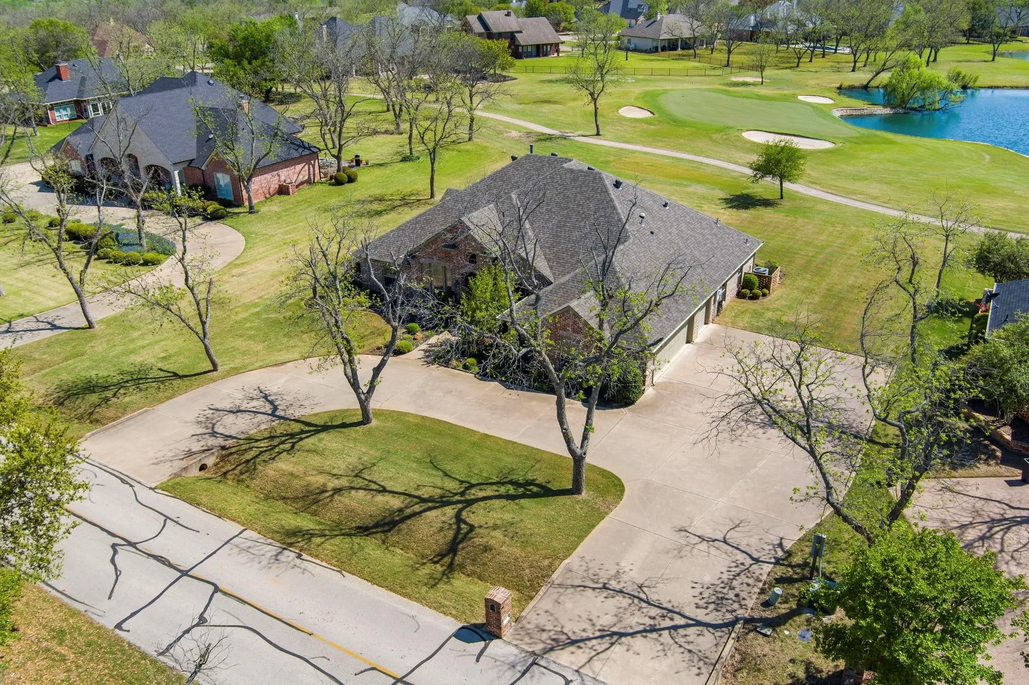Brick exterior residence with a multi-car garage, expansive driveway, and mature landscaping