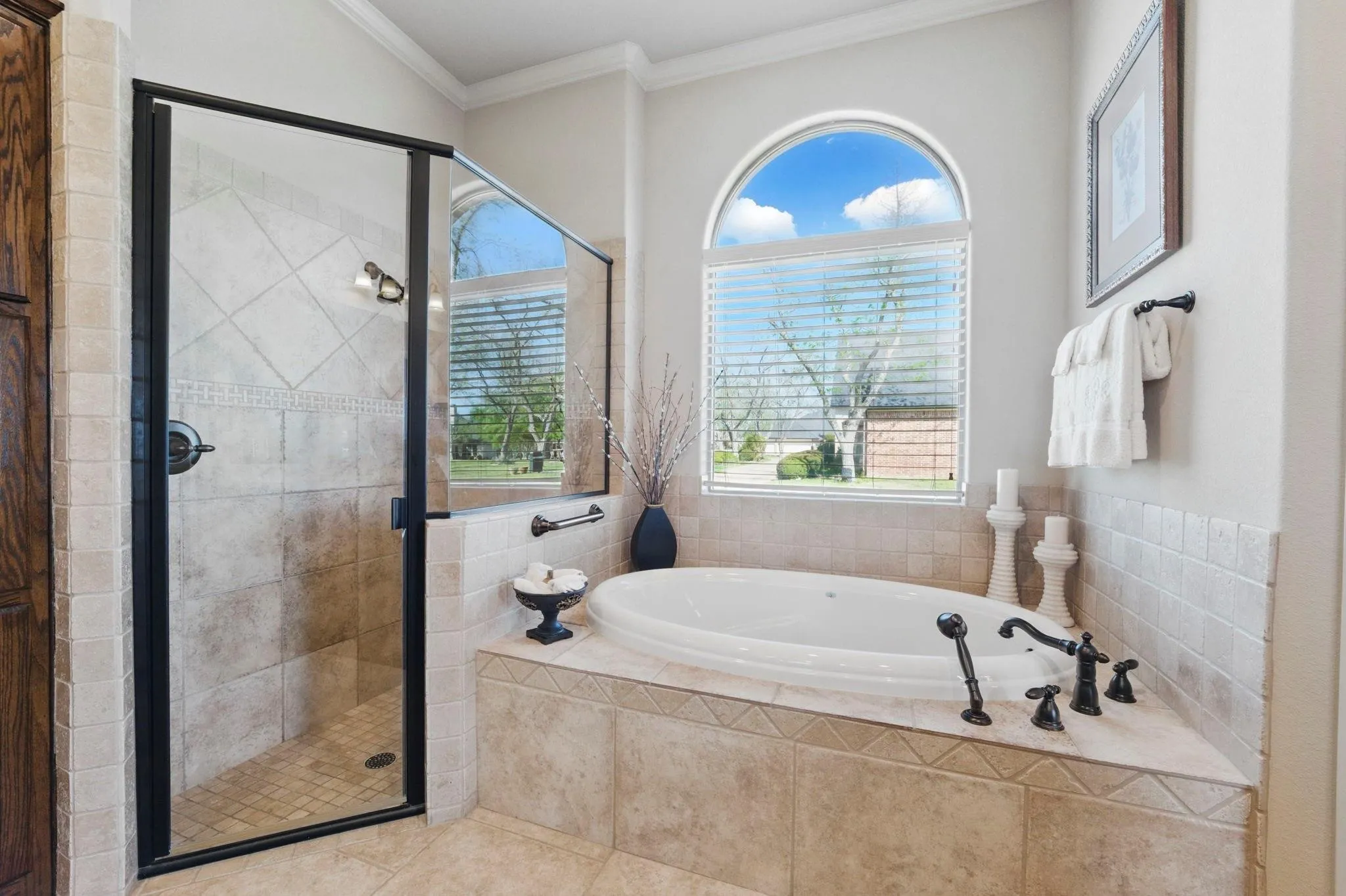 Soaking tub with dark bronze fixtures, an arched window, and tile surround