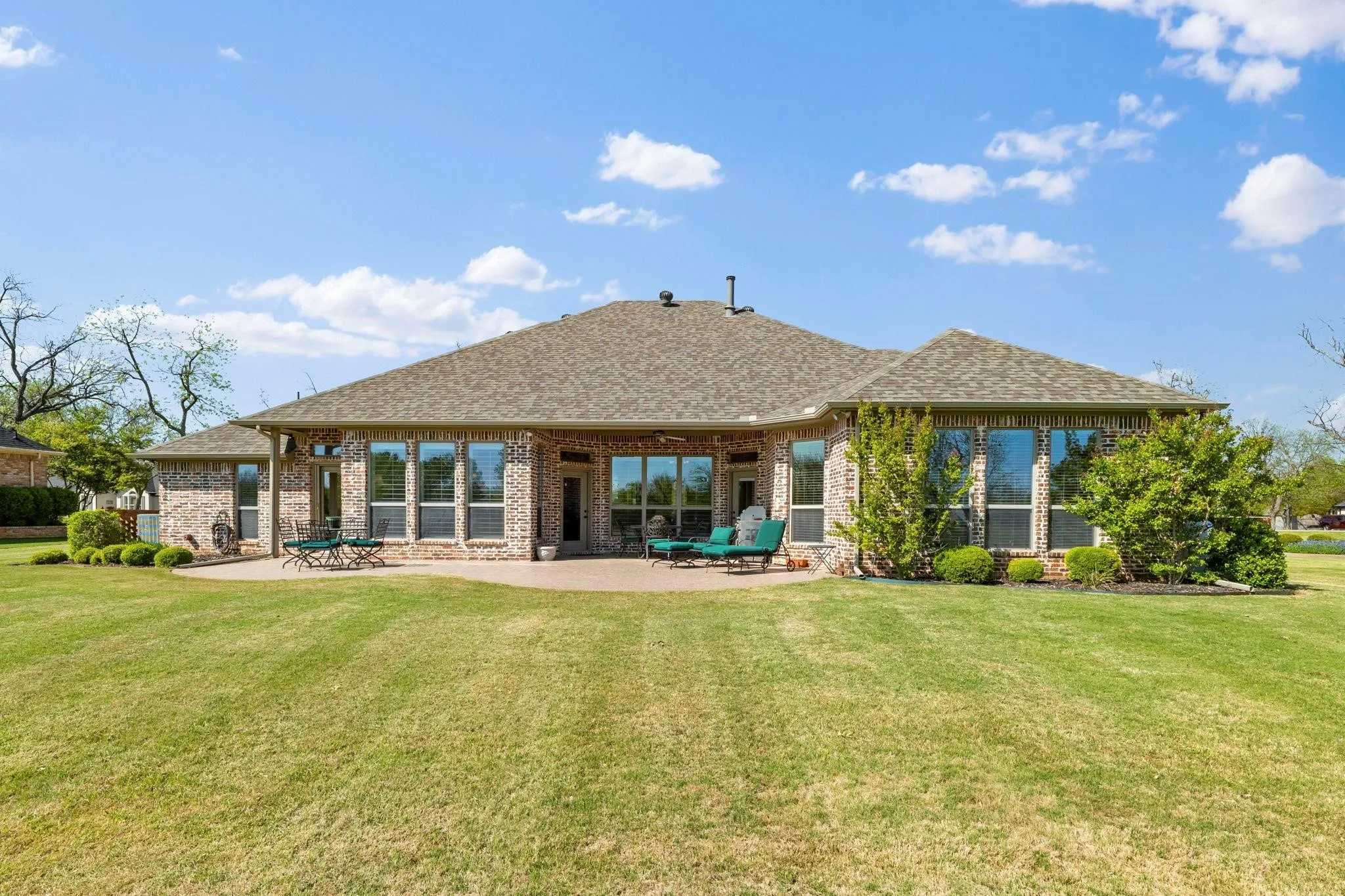 Brick exterior with multiple large windows, covered patio, and a spacious lawn