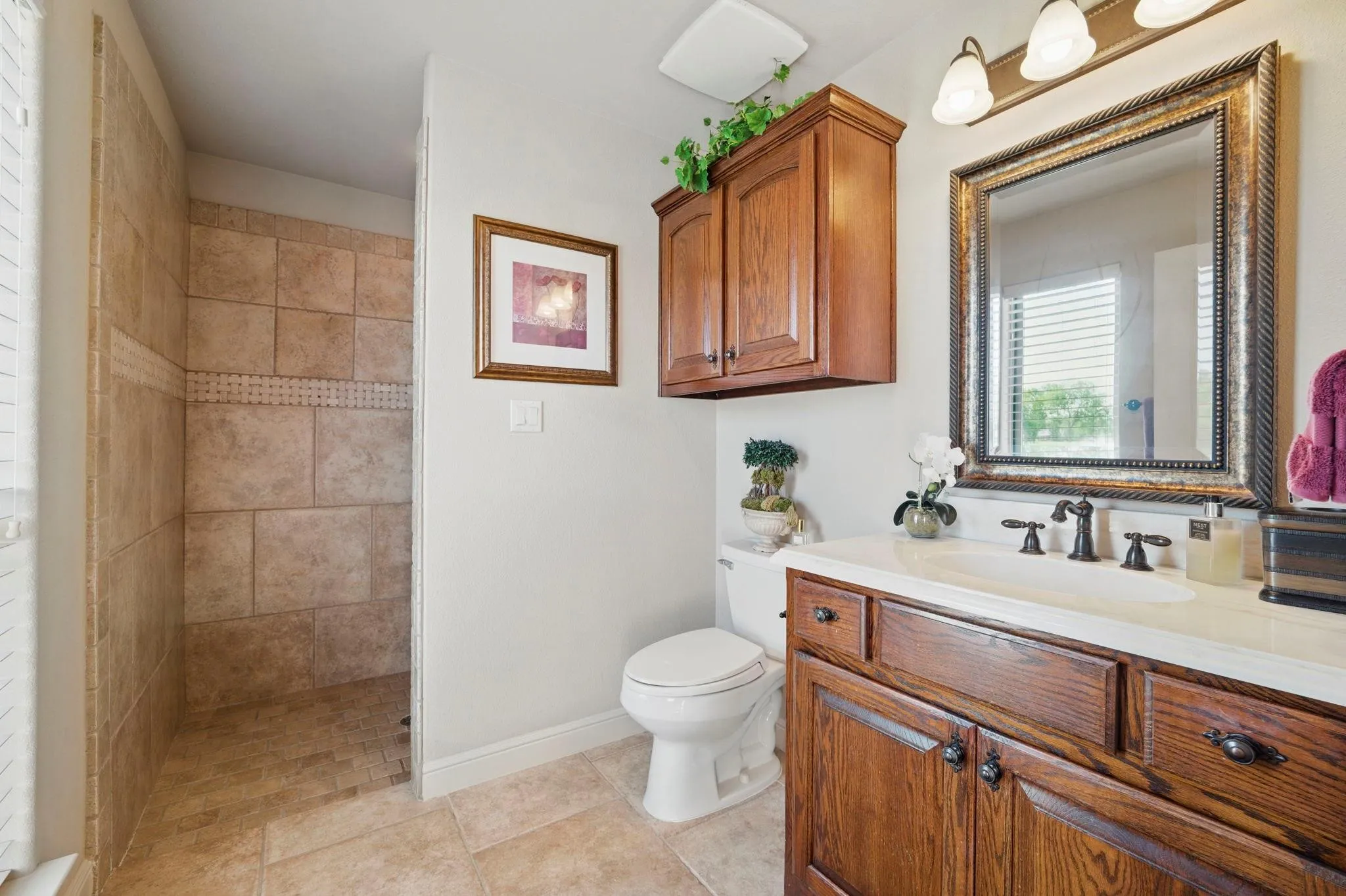 Tile-surrounded walk-in shower, wood-finish vanity with an integrated sink, framed mirror, and wall-mounted light fixture