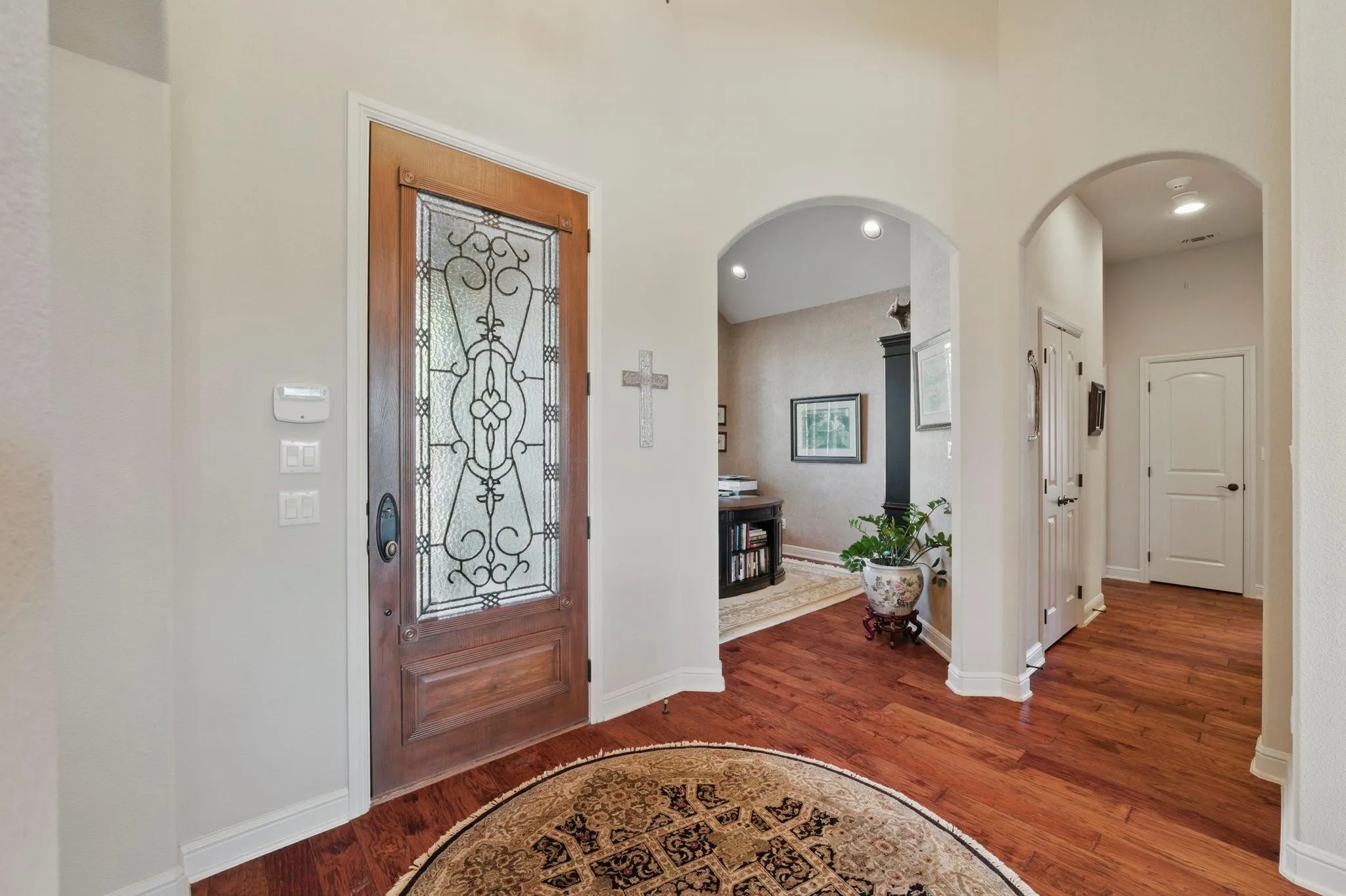 Wood-finish flooring throughout, featuring a solid wood door with decorative glass inlay, and arched doorways