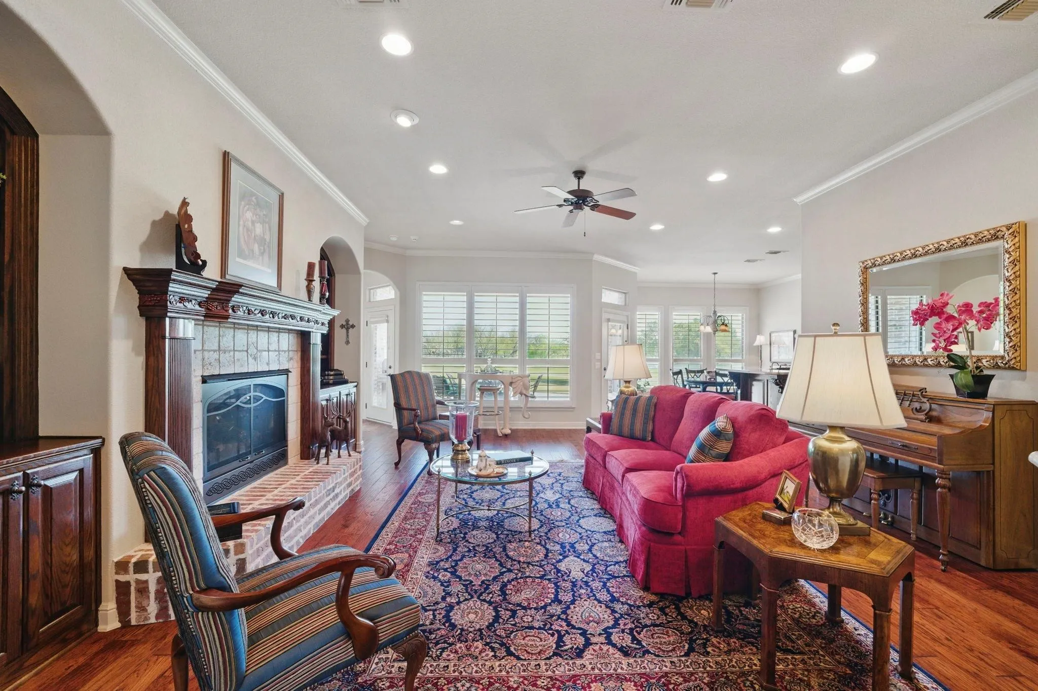 Hardwood flooring, crown molding, a fireplace with a detailed wood mantel and brick hearth, recessed lighting, and a ceiling fan