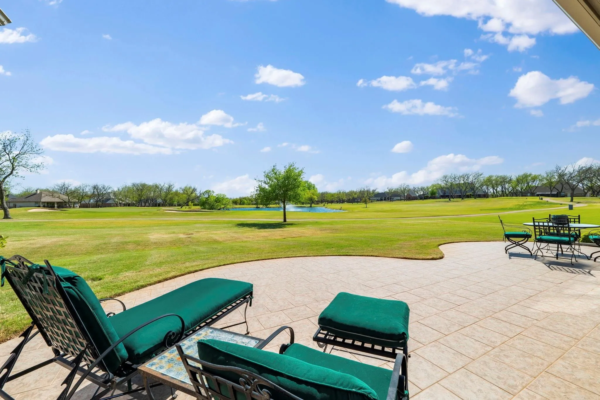 Expansive outdoor patio with a textured concrete surface, overlooking a lush green landscape and a water feature
