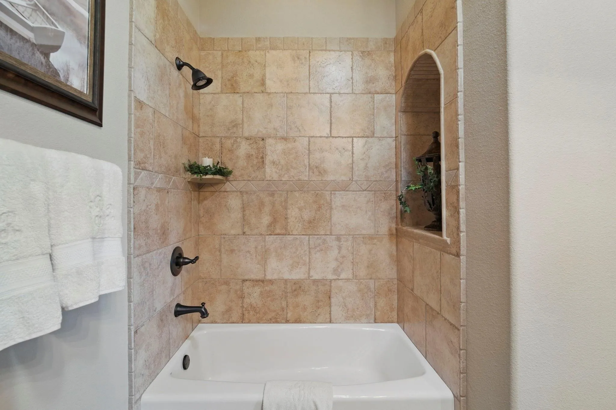 Bathtub with tiled surround, an arched recessed niche, and dark bronze fixtures