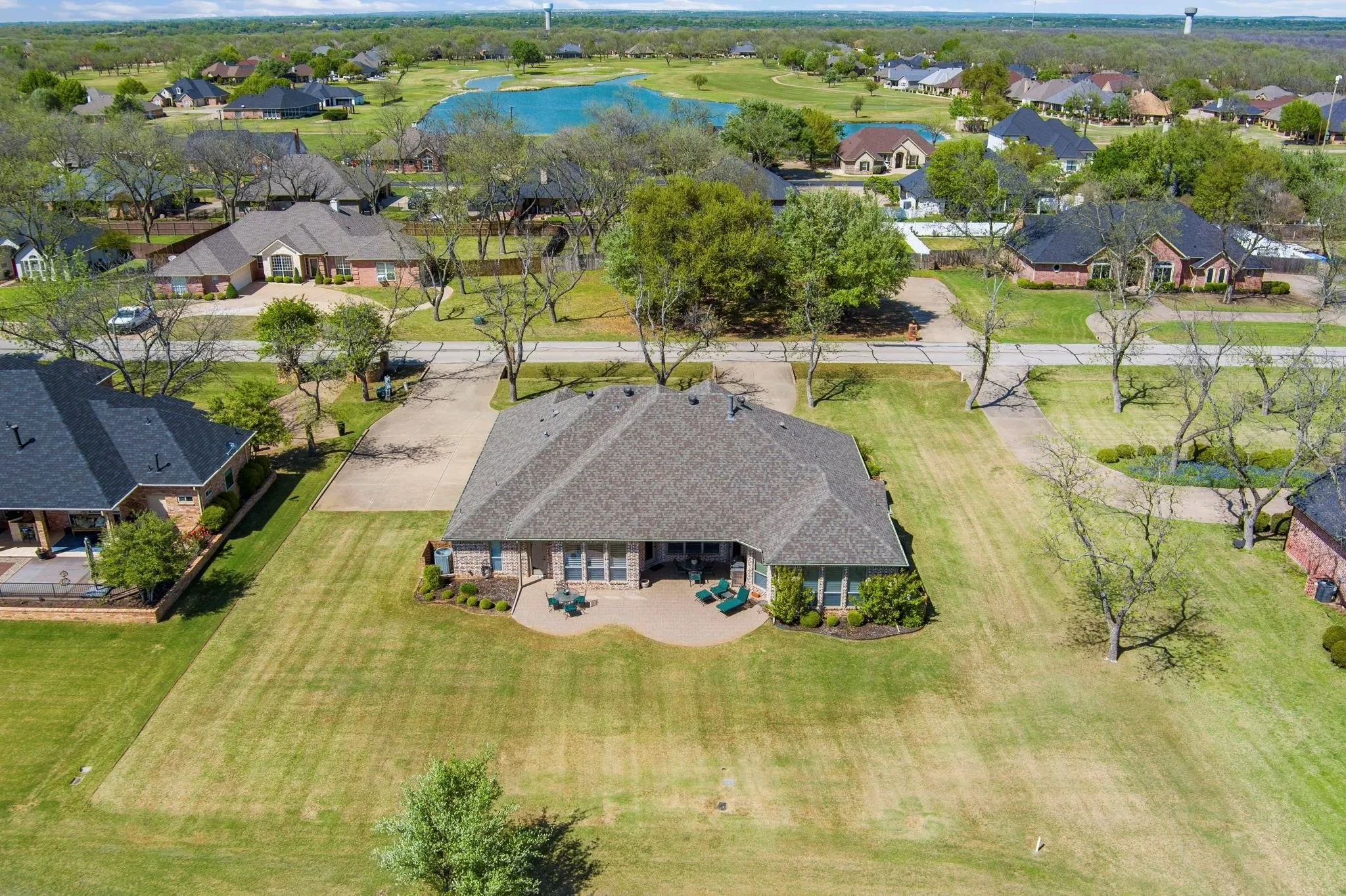 Expansive property featuring a paved driveway, a large backyard with a manicured lawn, an outdoor patio, and a shingled roof
