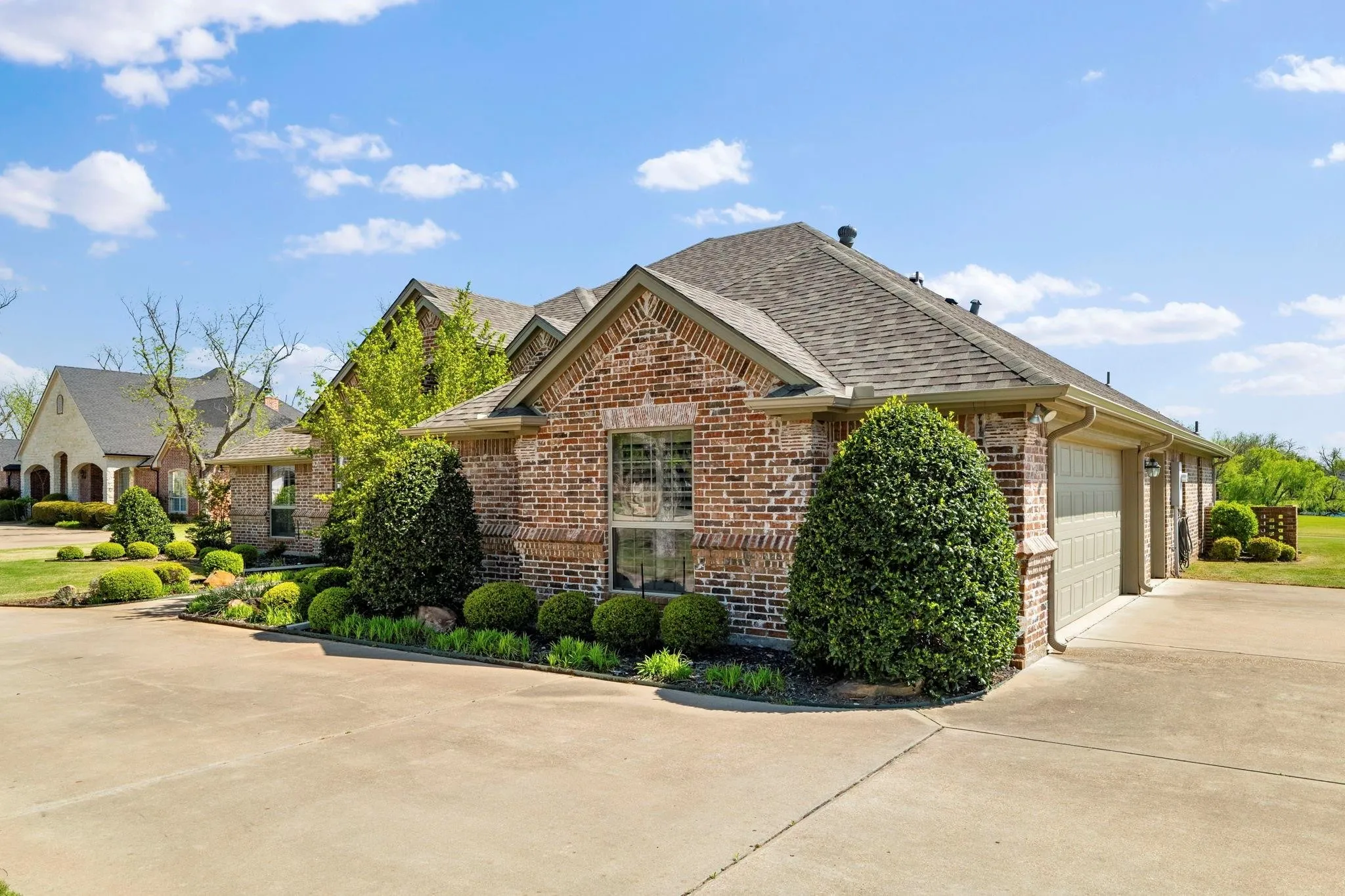 Brick exterior with gabled roofline, concrete driveway, and mature landscaping