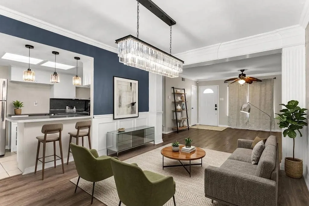 Open-concept living space featuring wood-finish flooring, a contemporary linear chandelier, and a kitchen pass-through with pendant lighting