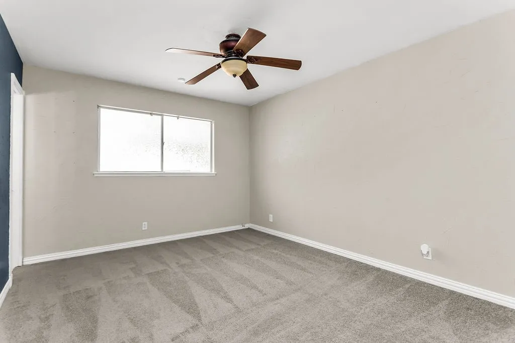 Carpeted room with a ceiling fan, light-toned walls, and a multi-pane window