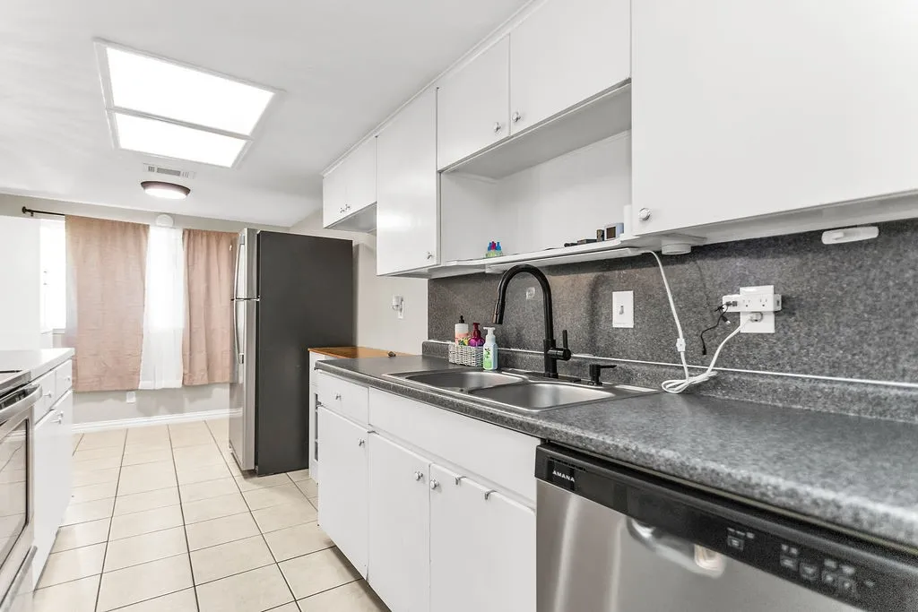 White cabinetry with chrome hardware, dual basin stainless steel sink, black-finish faucet, and tiled flooring