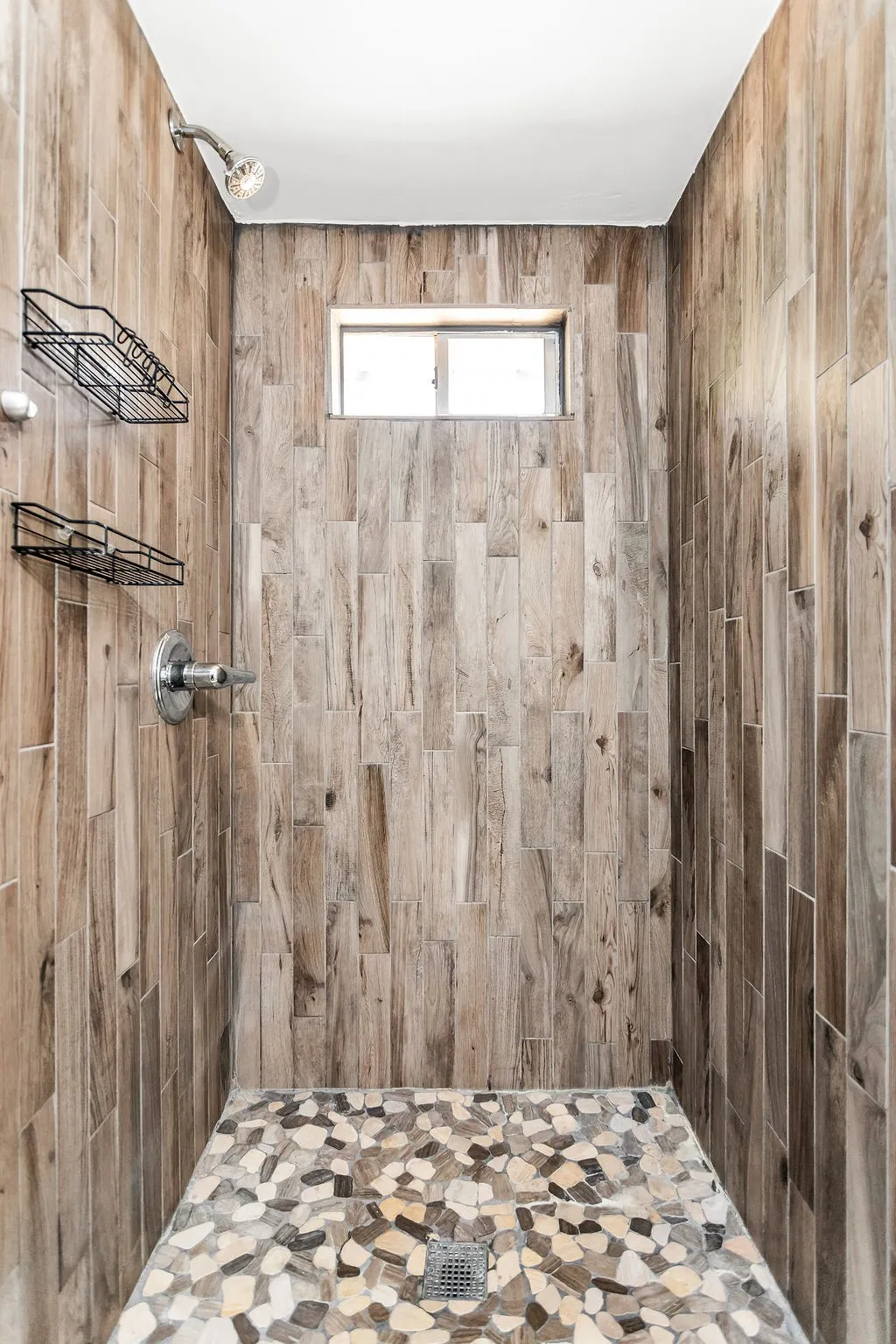 Shower featuring wood-finish wall tile, pebble-finish flooring, and a fixed window