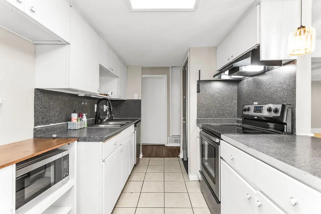 Galley kitchen featuring white cabinetry, dark speckled countertops, a stainless steel double basin sink with a black faucet, and a built-in electric range with an overhead vent hood