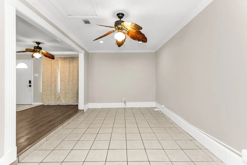 Tiled flooring paired with wood-finish flooring, crown molding, and two ceiling fans with integrated lighting