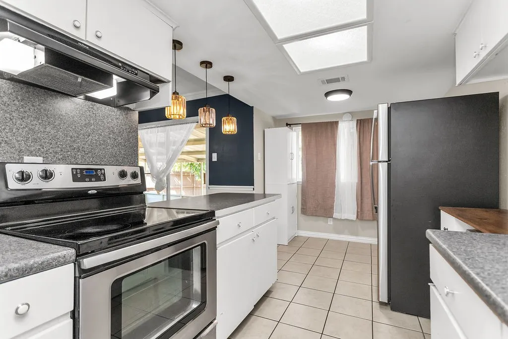 Kitchen featuring stainless steel range, white cabinetry, dark grey countertops, and neutral tile flooring