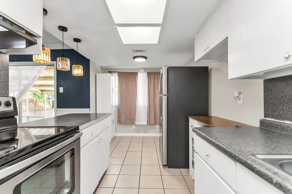 Galley kitchen featuring white cabinetry, dark speckled countertops, tile flooring, and stainless steel appliances