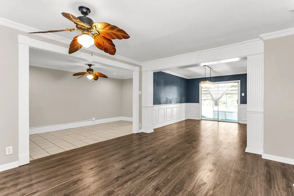 Wood-finish flooring, white decorative wainscoting, sliding glass doors, and a ceiling fan with light fixture