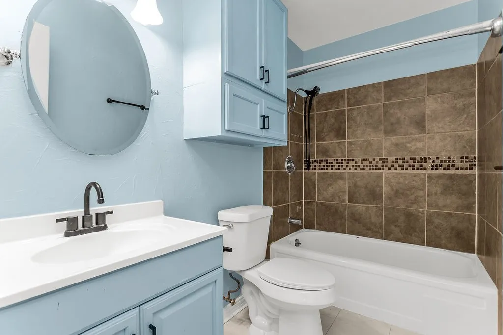 Bathroom featuring a vanity with an integrated sink, blue cabinetry, a wall-mounted mirror, a tub with a shower, and tiled shower walls
