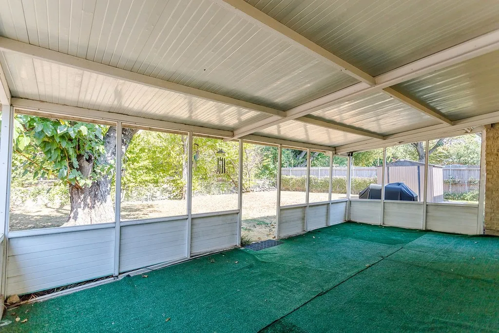 Expansive screened-in porch with a corrugated ceiling, green outdoor carpeting, and framed panels