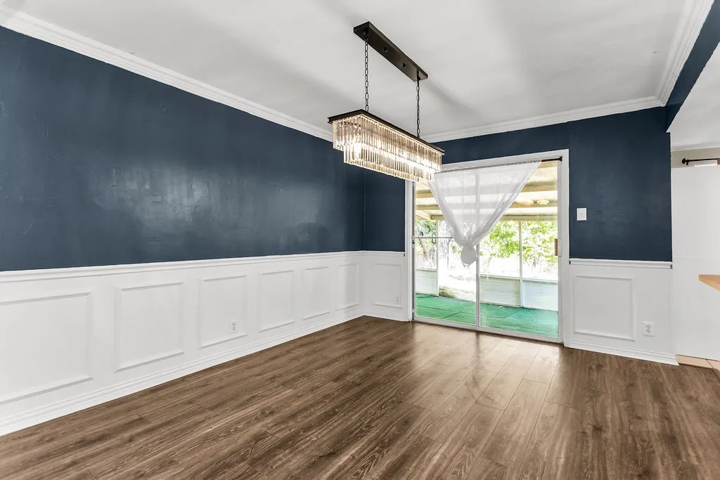 Wood-finish flooring, wainscoting, crown molding, a modern linear chandelier, and sliding glass doors