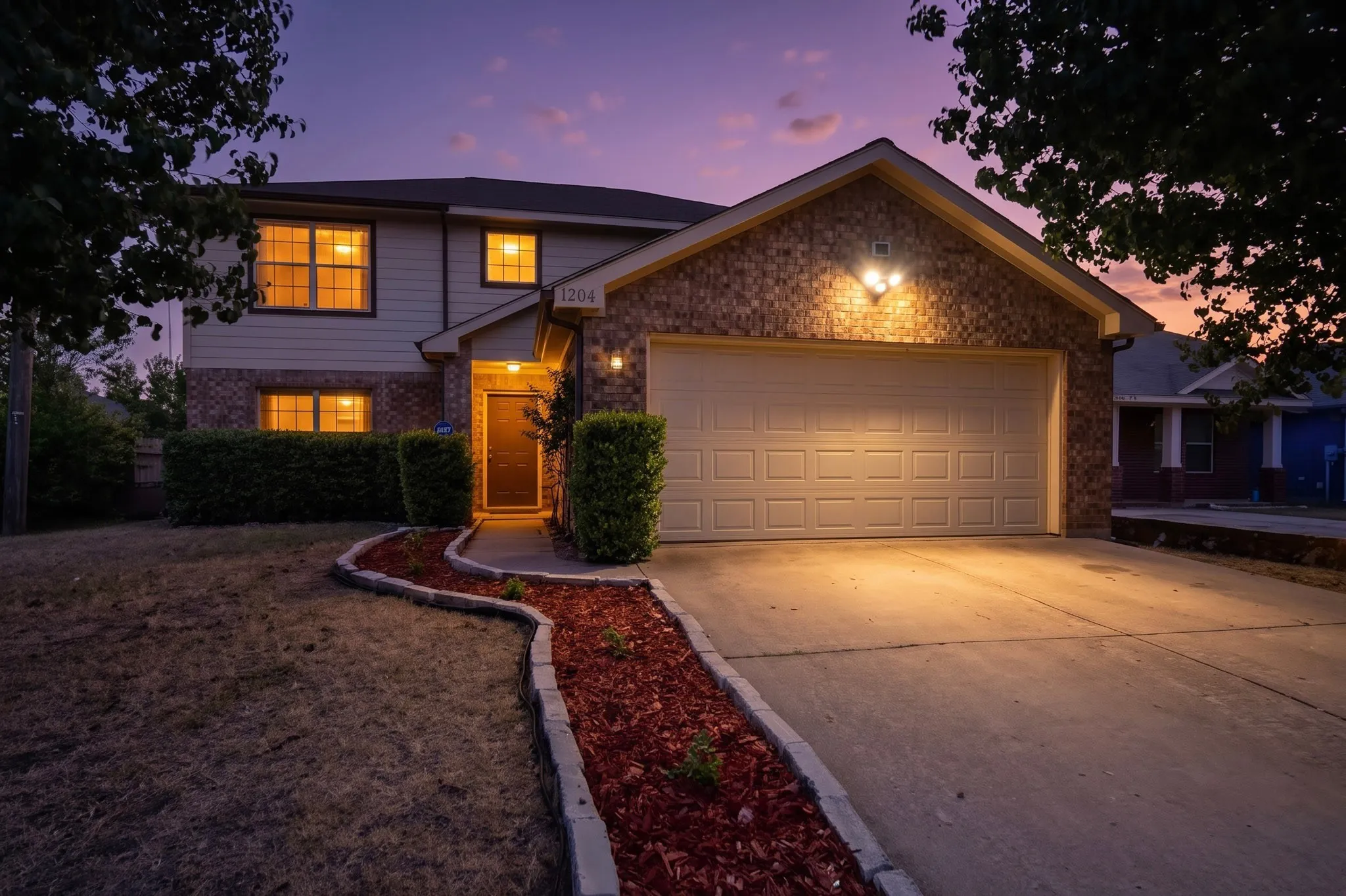 Two-story residence featuring a brick facade, attached two-car garage, concrete driveway, and a front walkway with decorative mulch beds