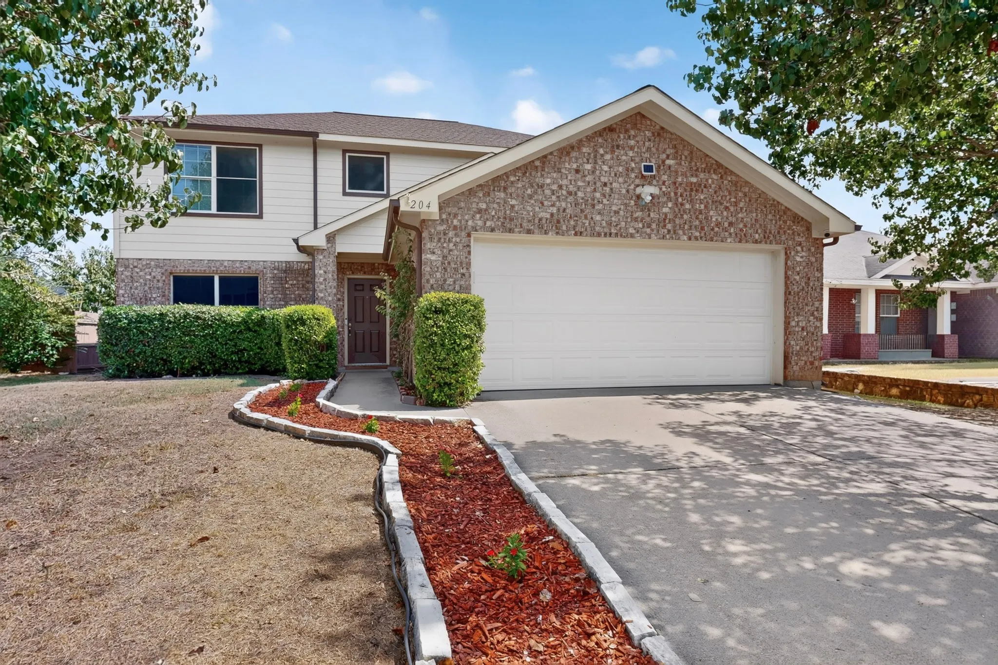 Brick and siding exterior, attached garage, concrete driveway, front walkway with stone edging, and mature landscaping