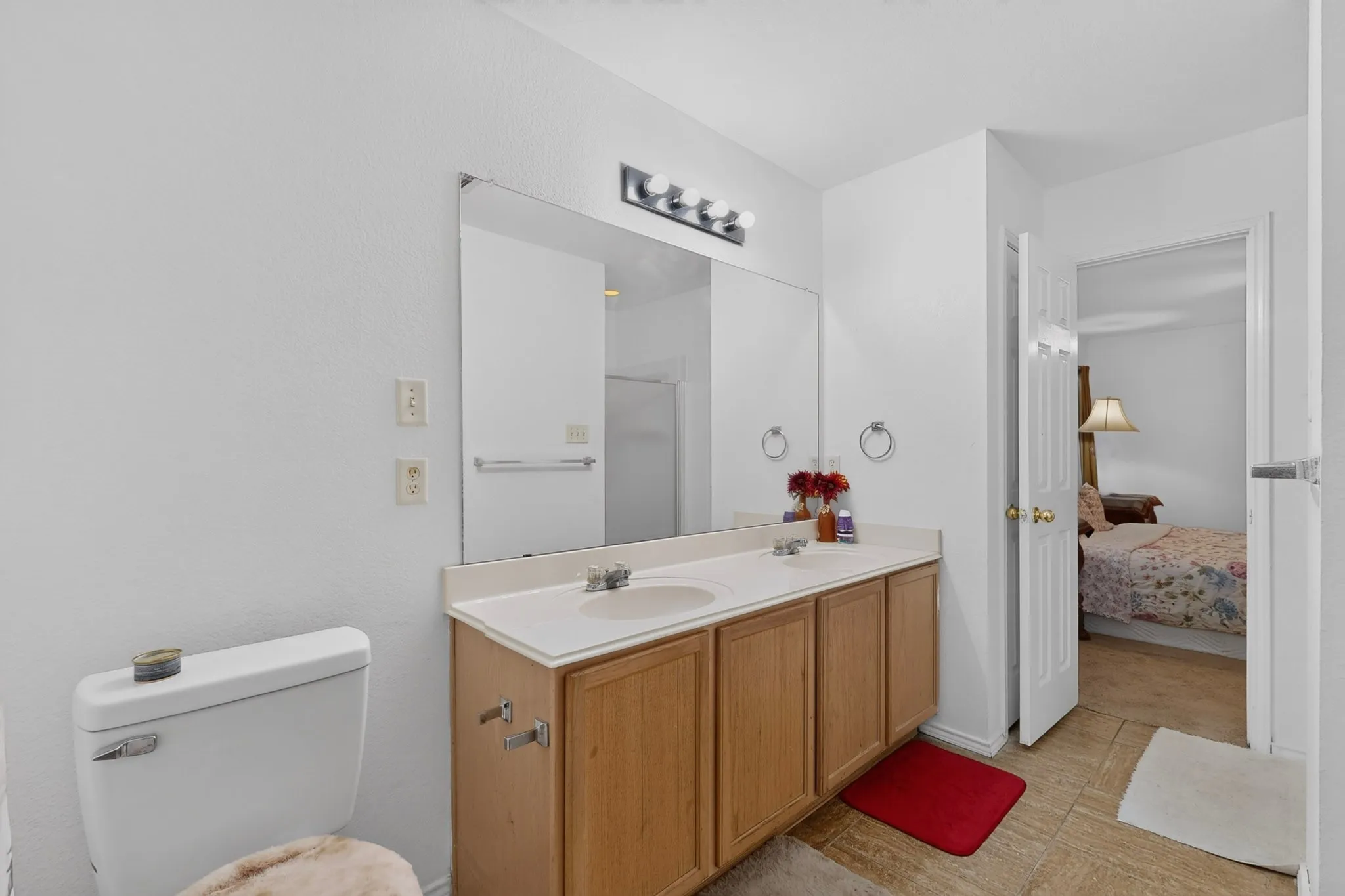 Dual sink vanity with light wood-finish cabinetry, a large wall-mounted mirror, and tile flooring