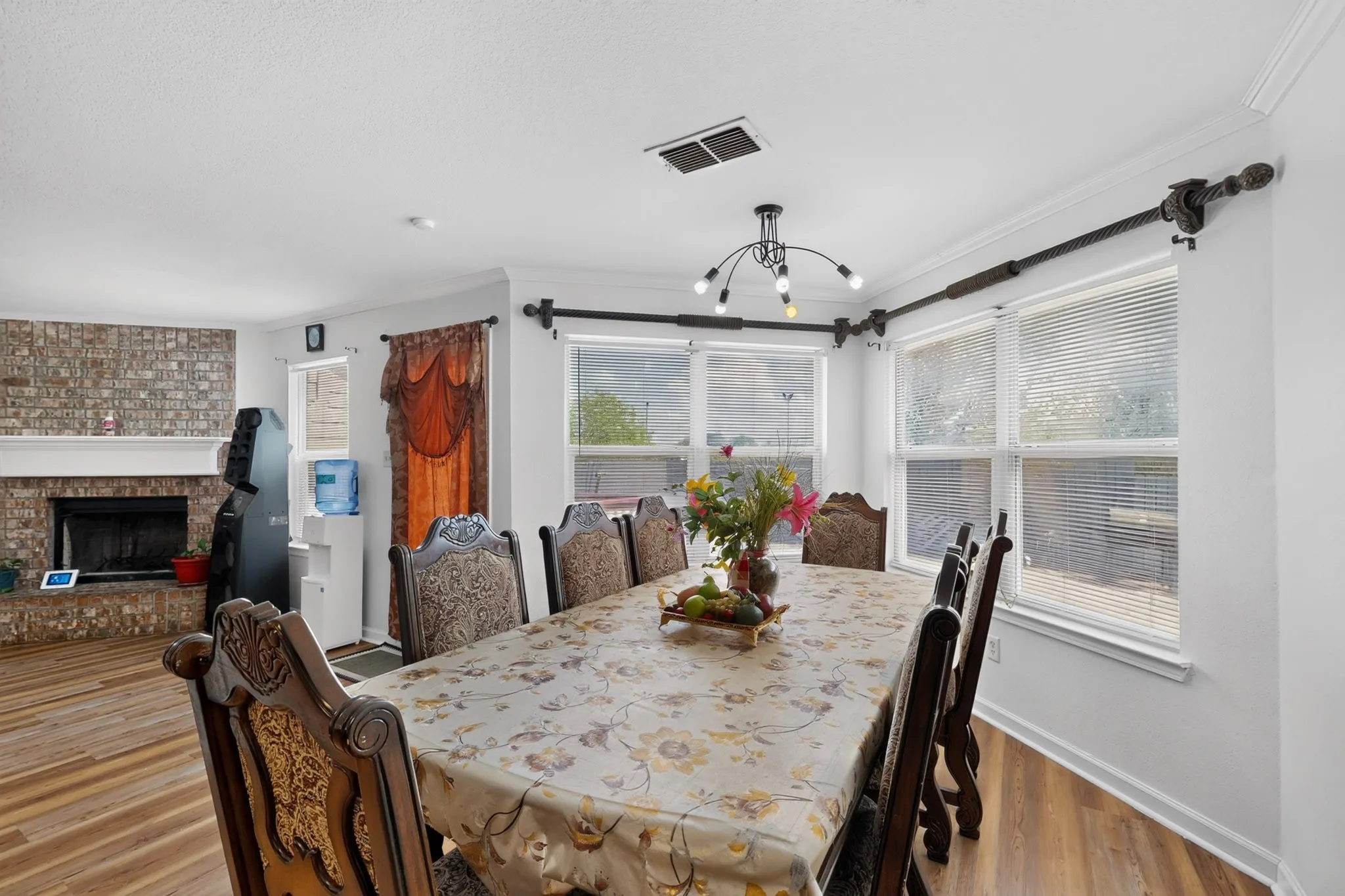Spacious room featuring wood-finish flooring, a corner brick fireplace with mantel, crown molding, and multiple windows