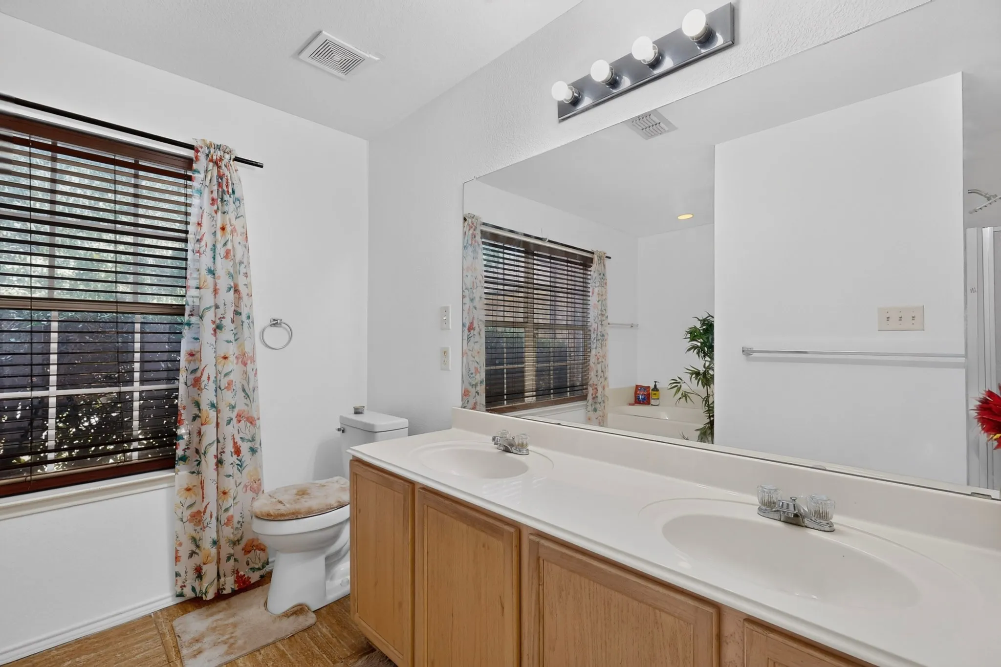 Dual vanity with integrated sinks, wood-finish cabinetry, and a large wall-mounted mirror