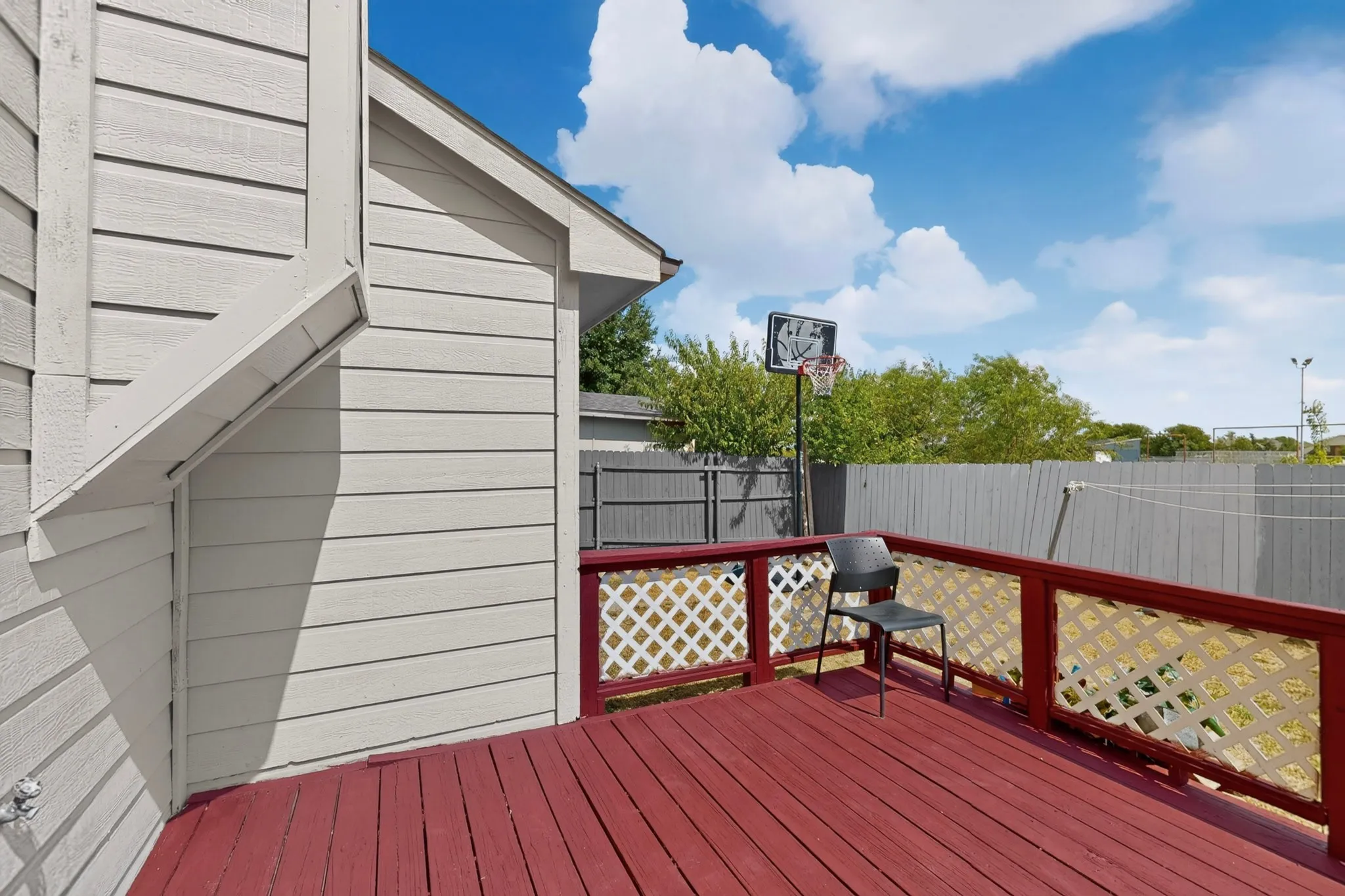 Outdoor deck with red-stained wood flooring, white lattice railing, and a privacy fence