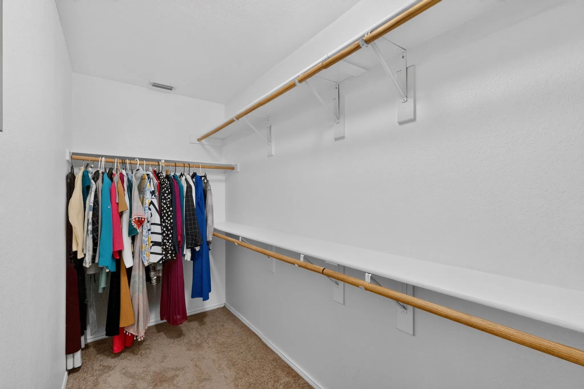 Walk-in closet featuring carpet flooring, upper and lower wood rods, and shelving