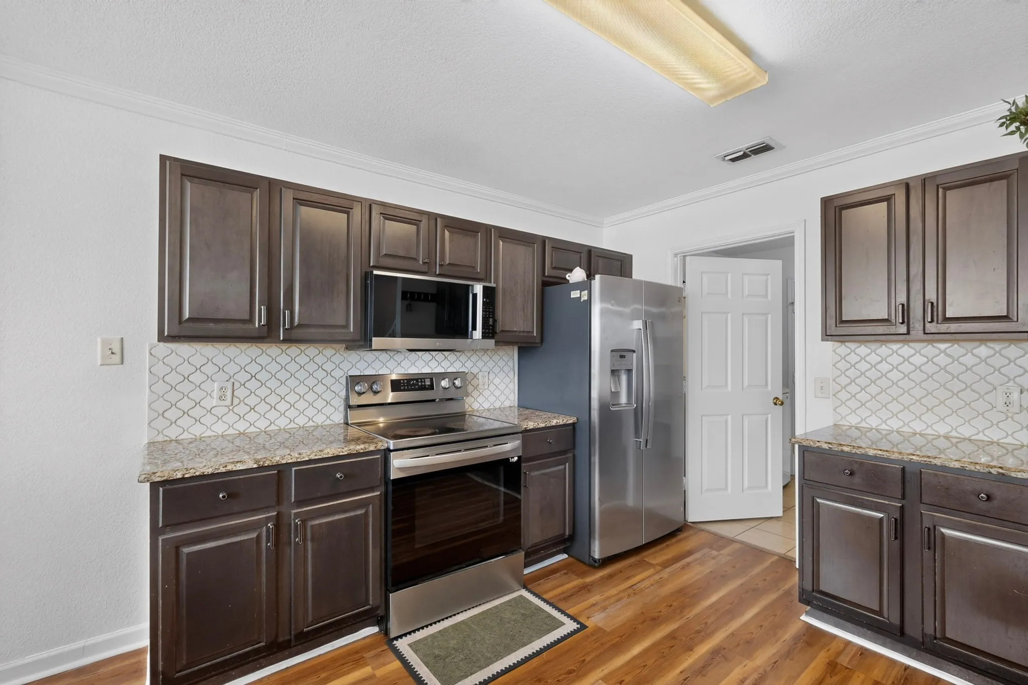 Kitchen featuring wood-finish flooring, dark wood cabinetry, granite countertops, and a decorative tile backsplash