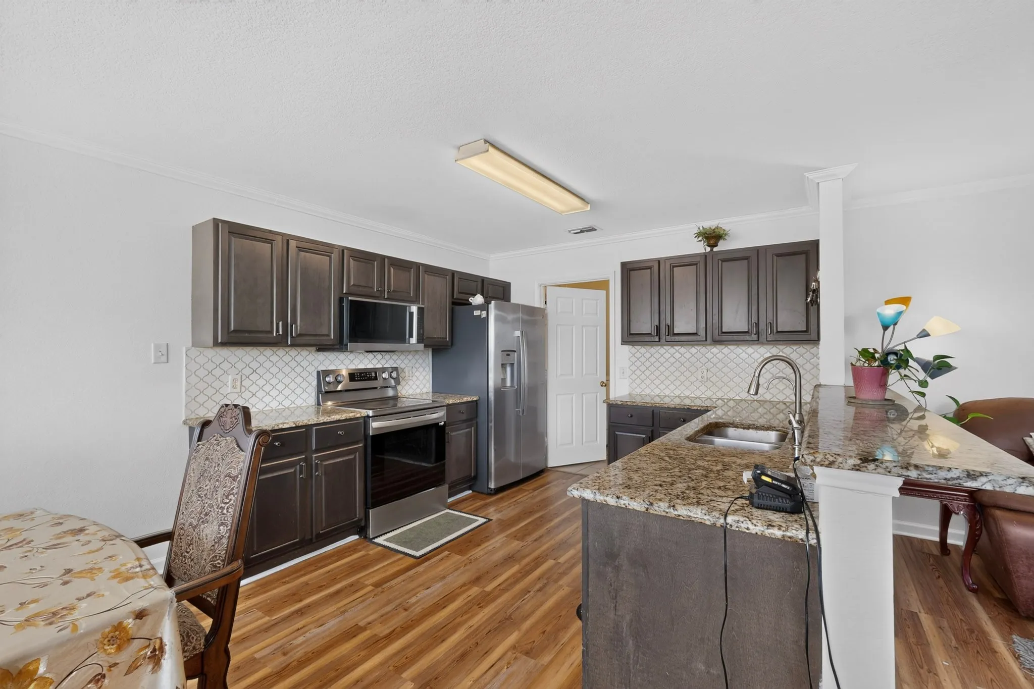 Kitchen featuring dark wood-finish cabinetry, light speckled countertops, a patterned tile backsplash, stainless steel appliances, and wood-finish flooring