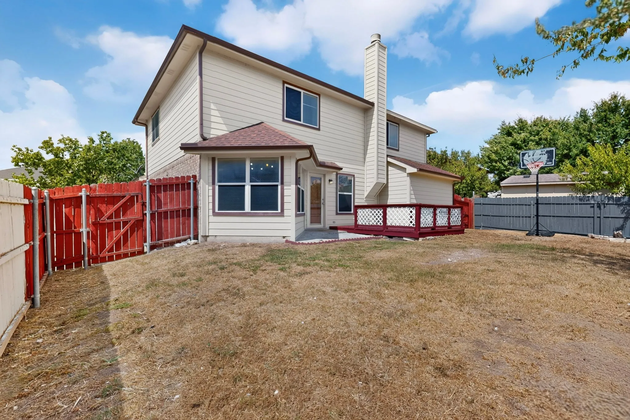 Expansive rear yard with a red-stained wooden deck featuring lattice railing, and a covered patio area