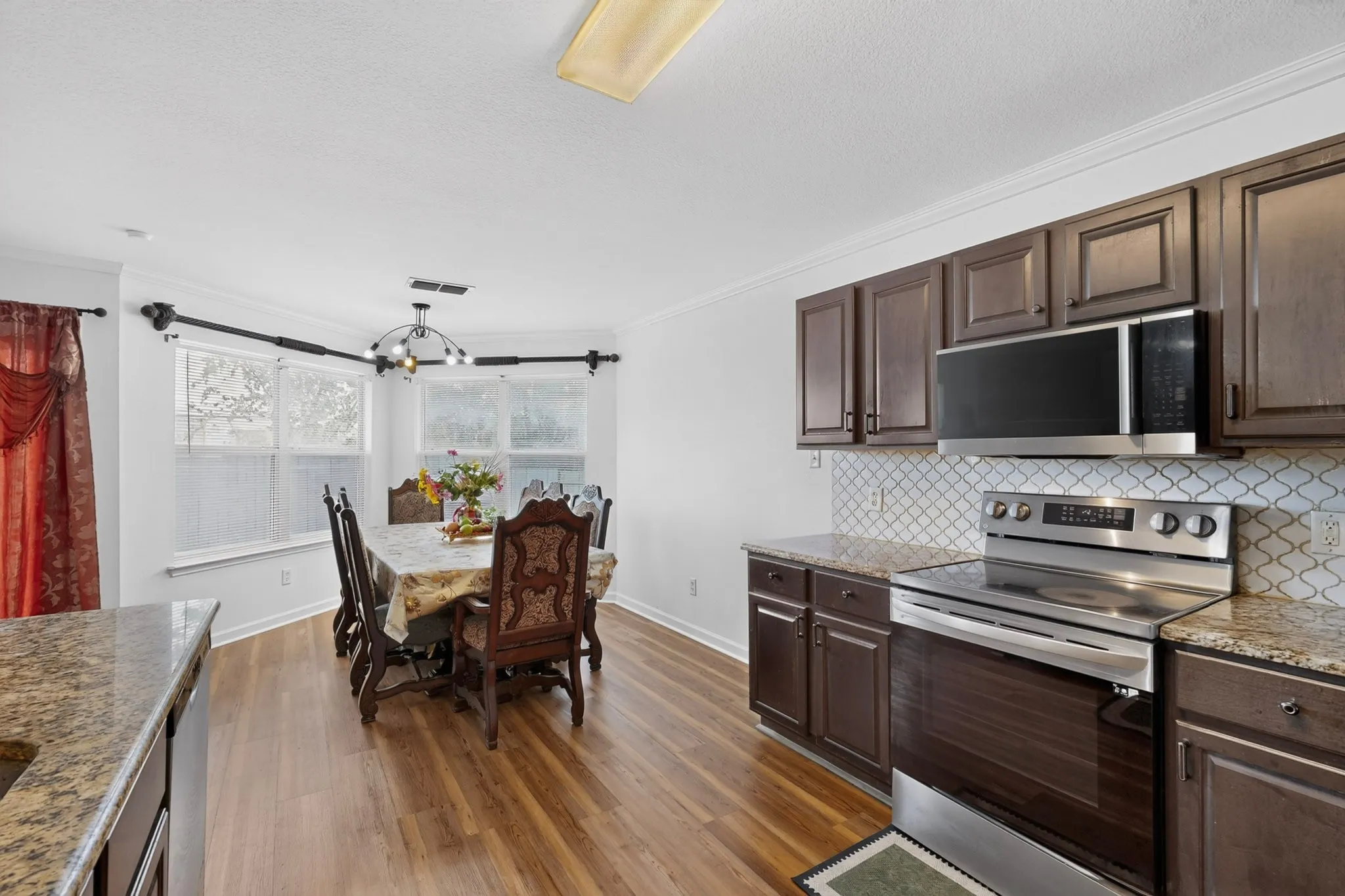 Kitchen and dining area featuring wood-finish flooring, dark wood cabinetry, stainless steel appliances, and a tiled backsplash