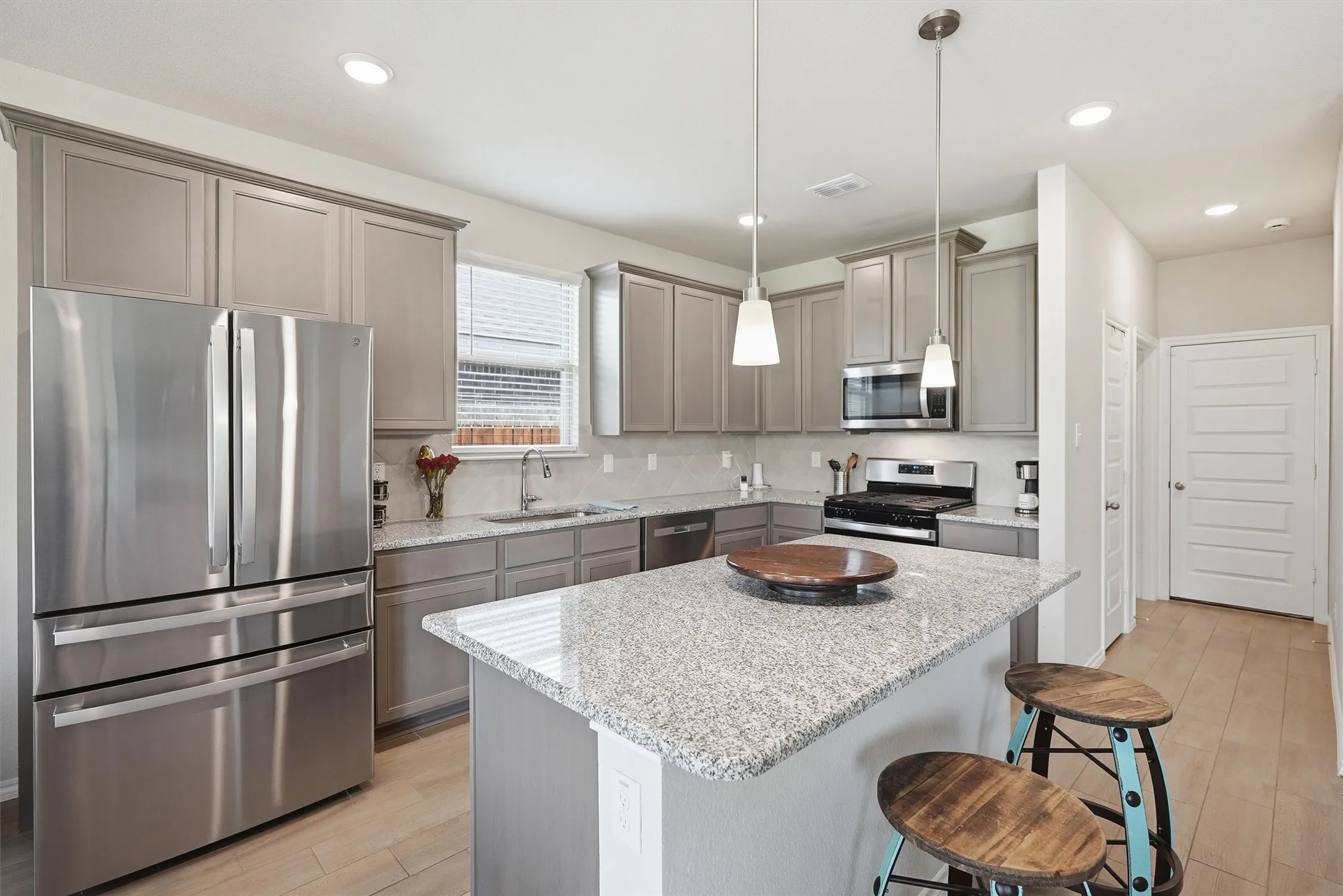 This bright filled kitchen features a window over the sink and a modern tile backsplash that perfectly complements the neutral color palette. The breakfast bar seating offers a casual spot for morning coffee, making this the true heart of the home.