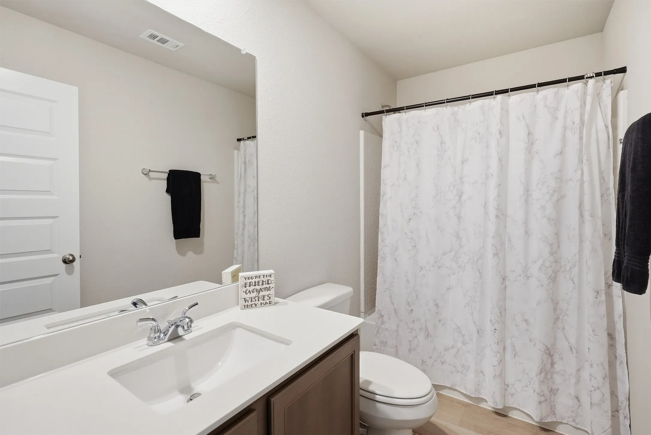 This bright quest bath features a modern vanity with integrated cabinetry and a crisp, white countertop for a polished look. The high ceilings and expansive mirror create an airy feel, ensuring a comfortable experience for family or visitors.