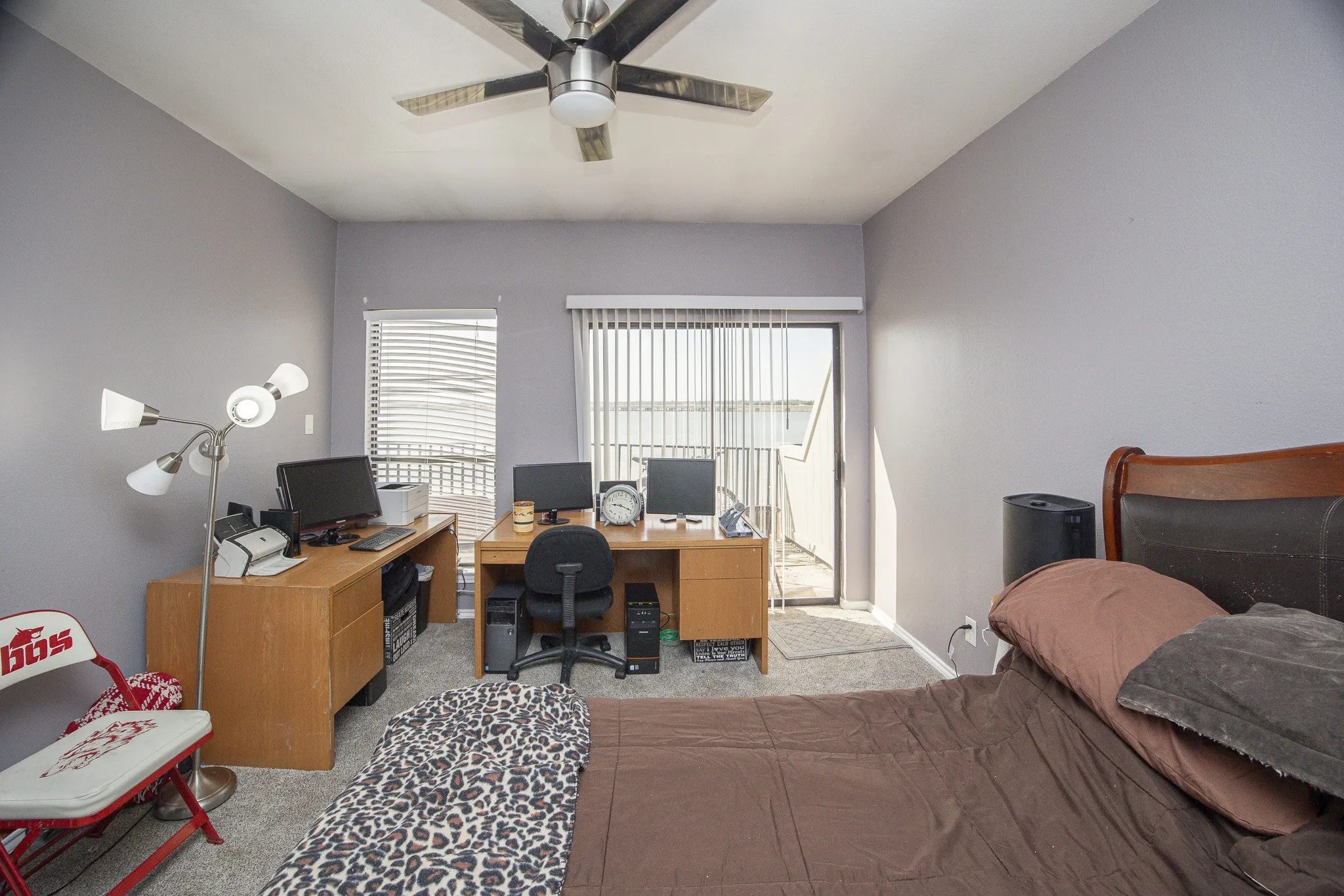 Neutral wall paint, ceiling fan with integrated lighting, two windows with horizontal blinds, glass sliding door, and carpeted flooring