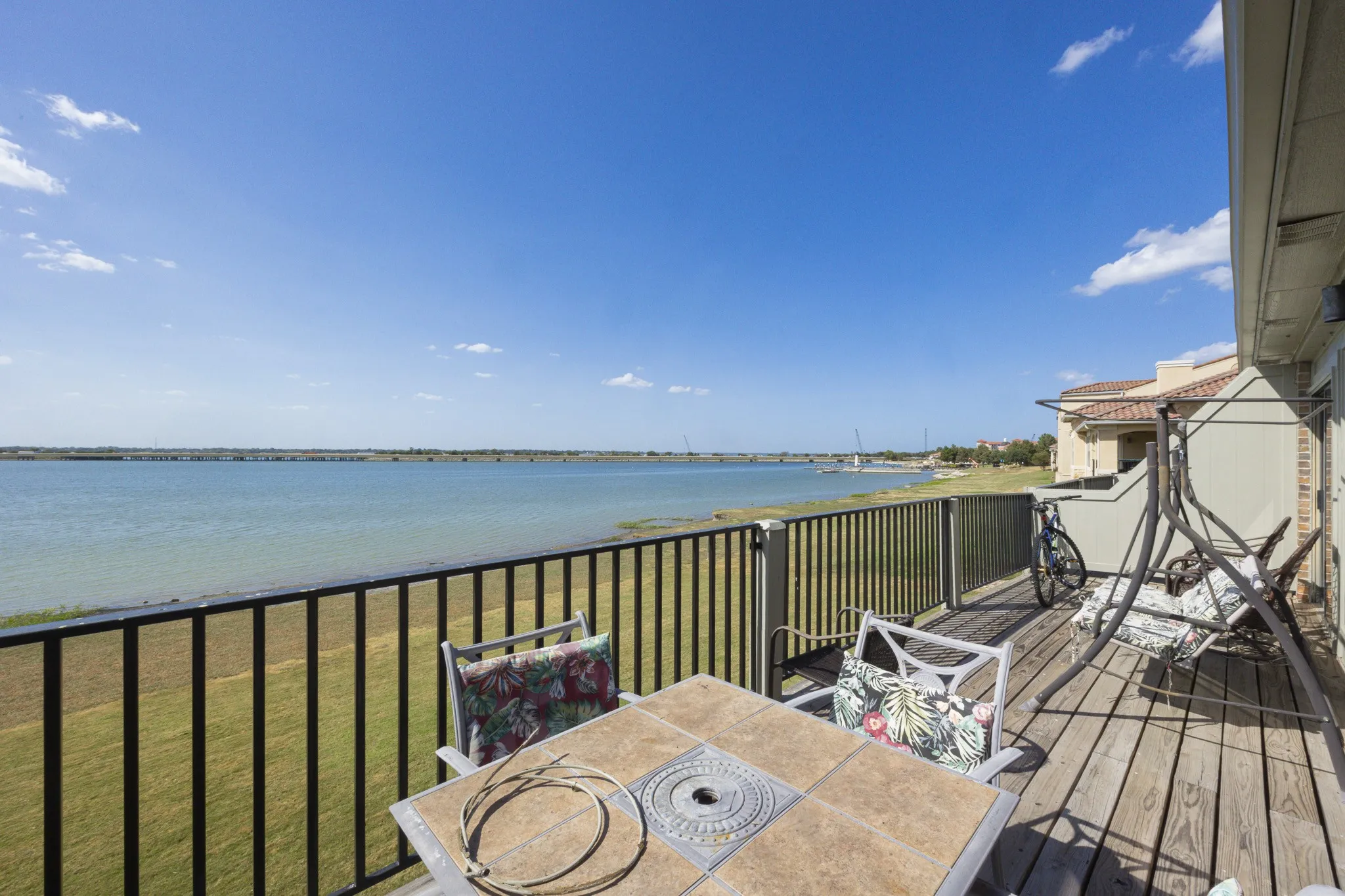 Expansive outdoor deck with wood-finish flooring, black metal railings, and waterfront scenery