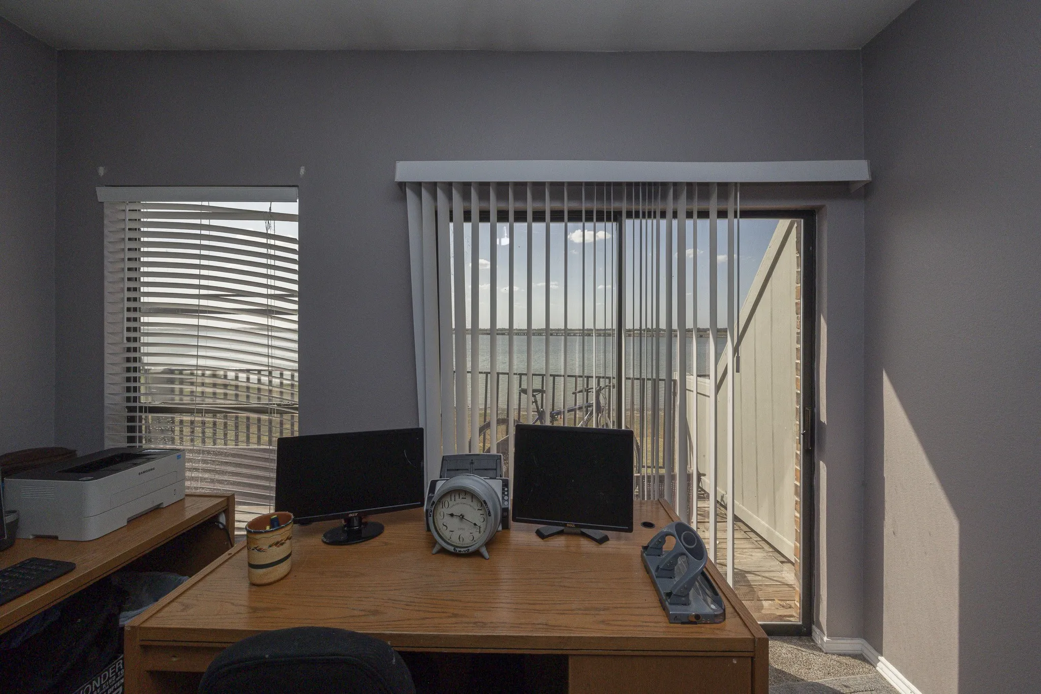 Sliding glass patio door with vertical blinds, private balcony, and wood-finish desk