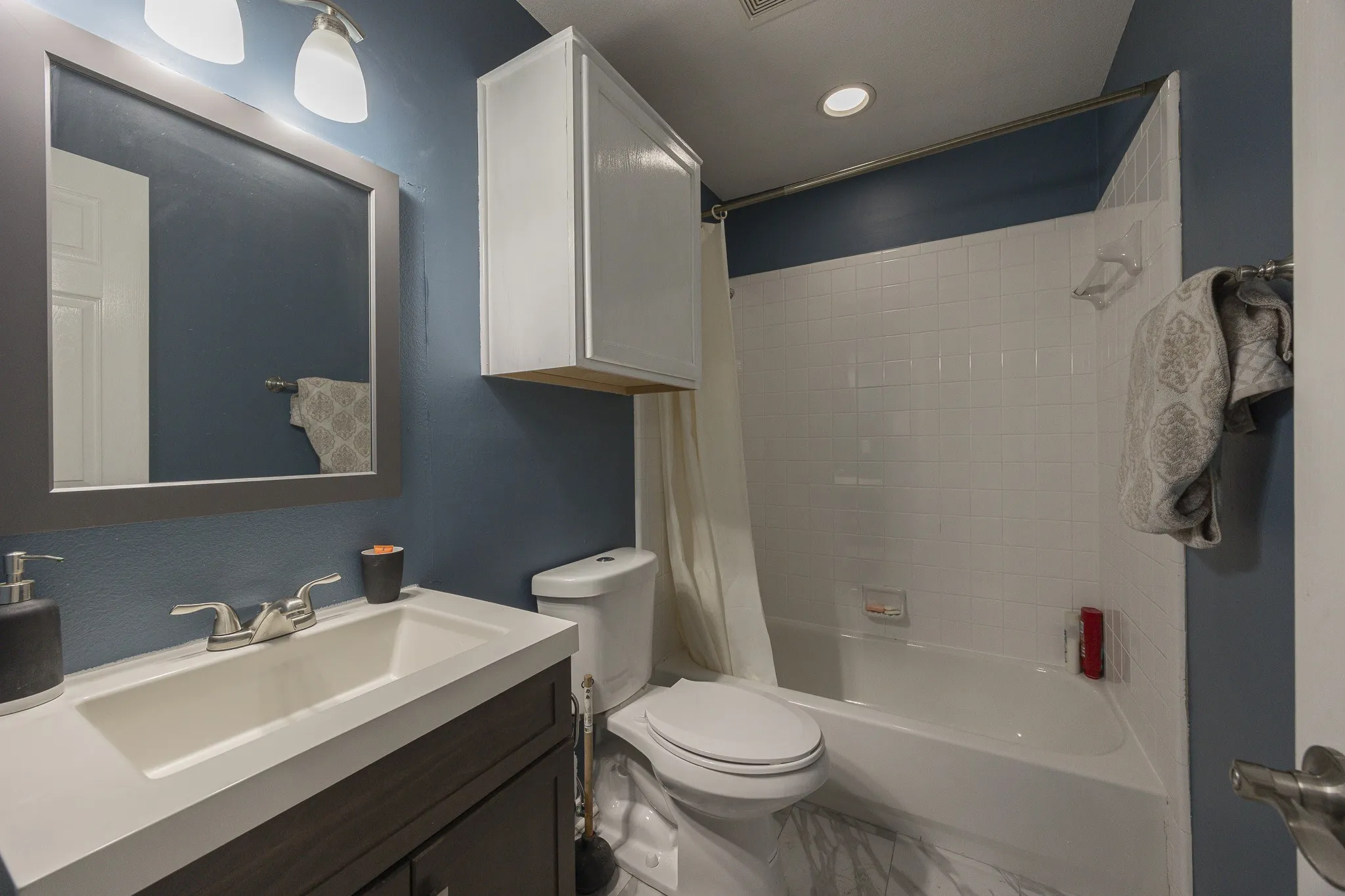 Vanity with an integrated sink, framed wall mirror, built-in storage cabinet, and a tiled shower-tub combination
