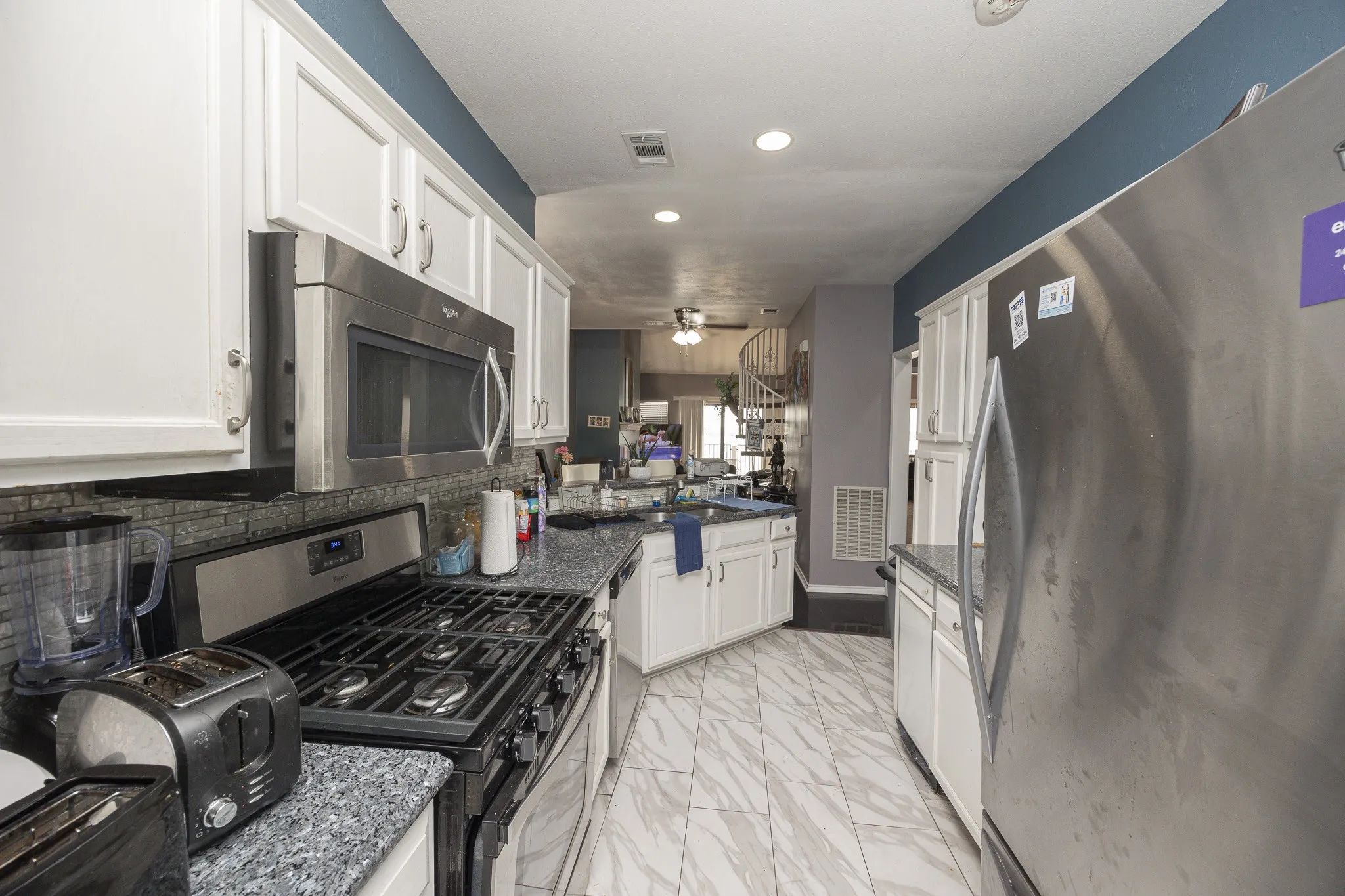 White shaker-style cabinetry, stainless steel appliances, dark stone countertops, tile backsplash, and light-toned tile flooring