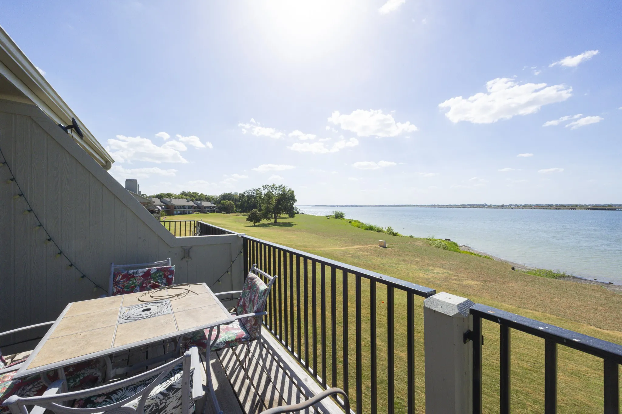 Balcony with black metal railing overlooking a body of water and expansive green space