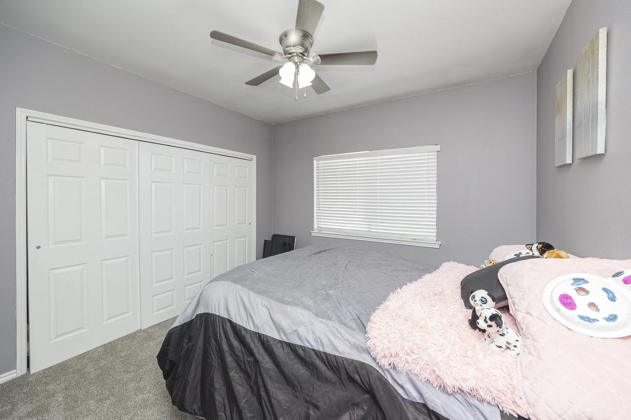 Room featuring neutral wall paint, a ceiling fan with integrated lighting, a window with horizontal blinds, and a built-in closet with paneled bifold doors