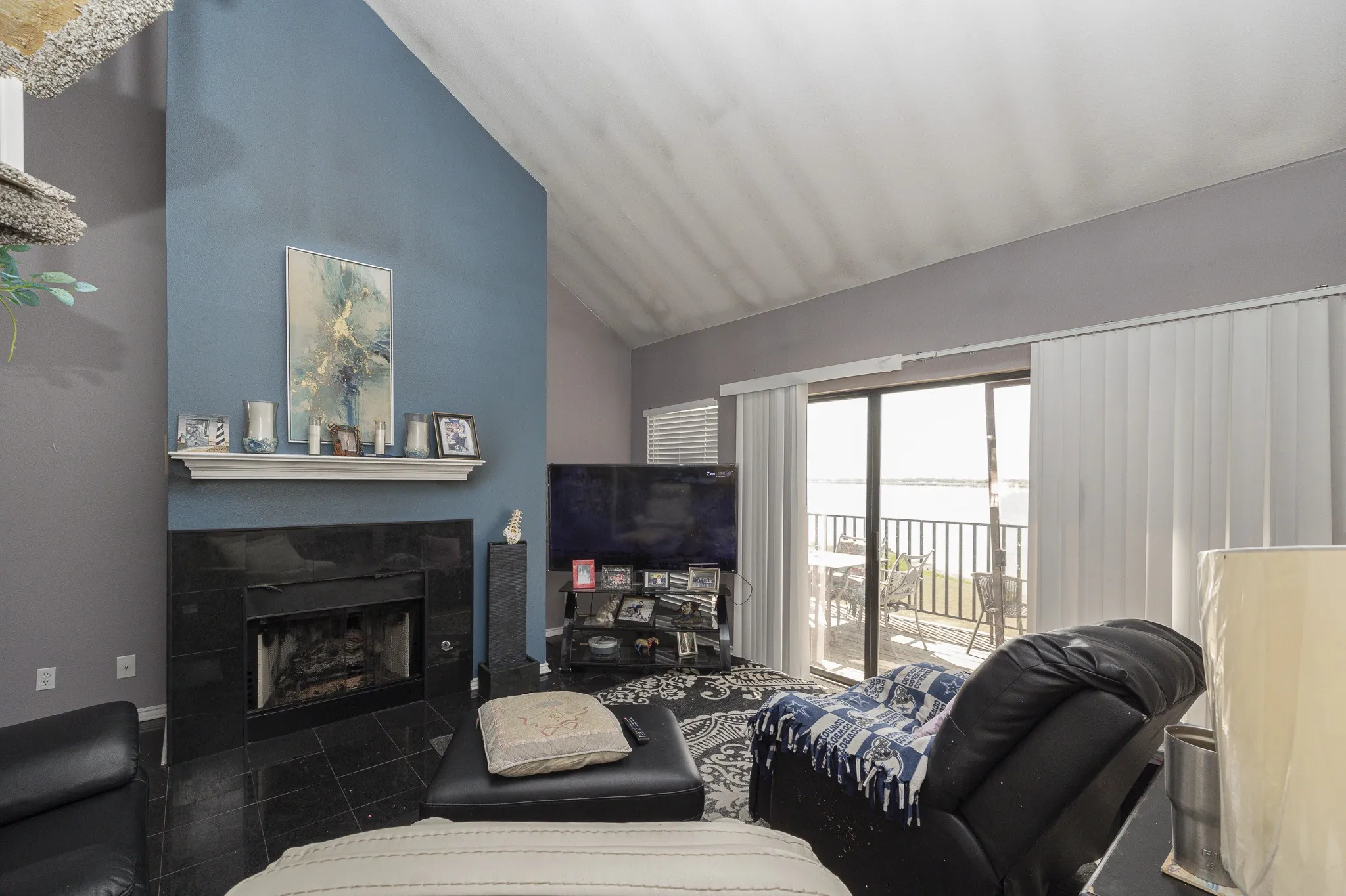 Vaulted ceiling living area featuring a black tile fireplace with white mantel, a sliding glass door, and an exterior balcony