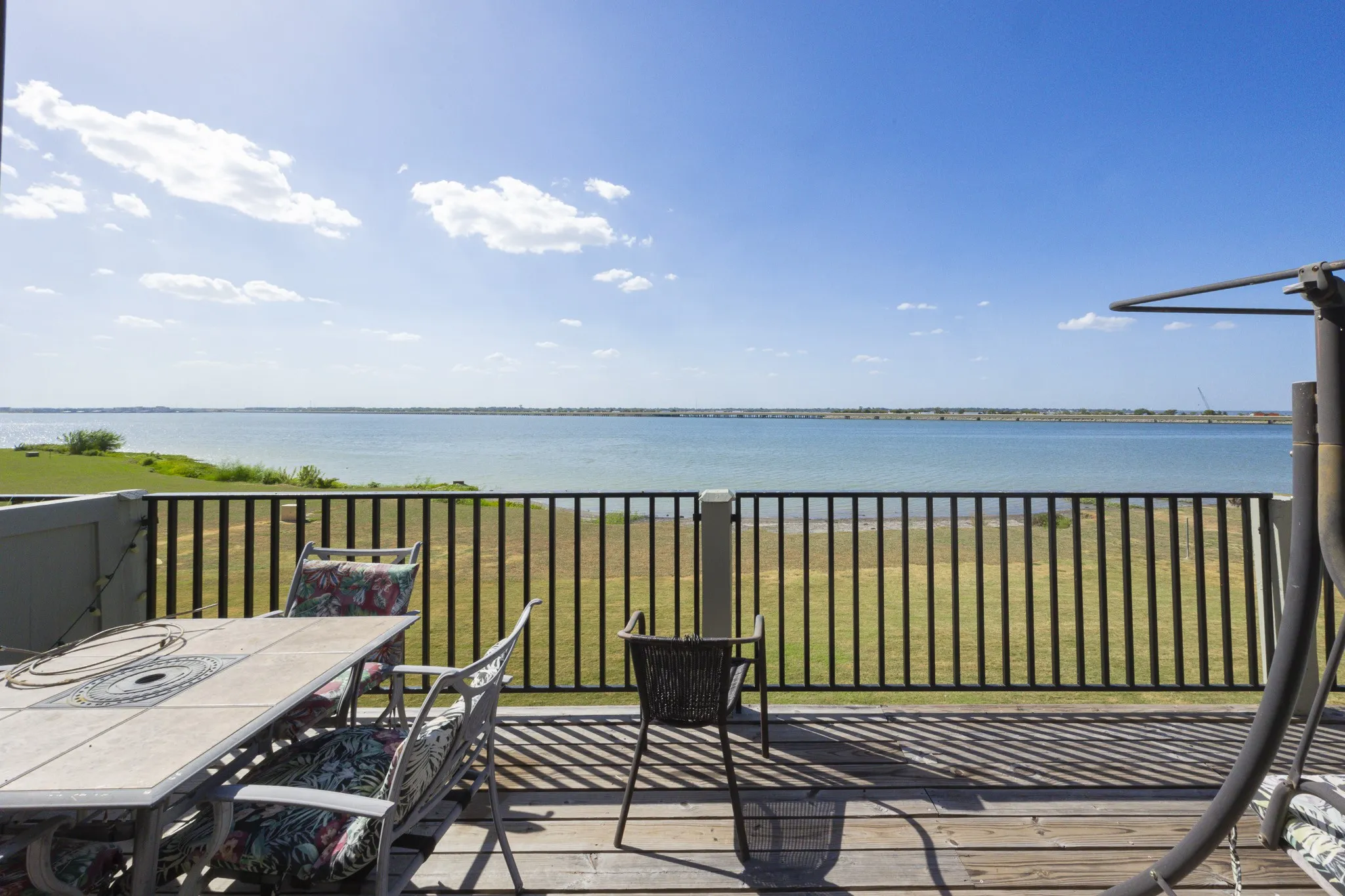 Expansive wood-finish deck with black metal railing overlooking a large body of water