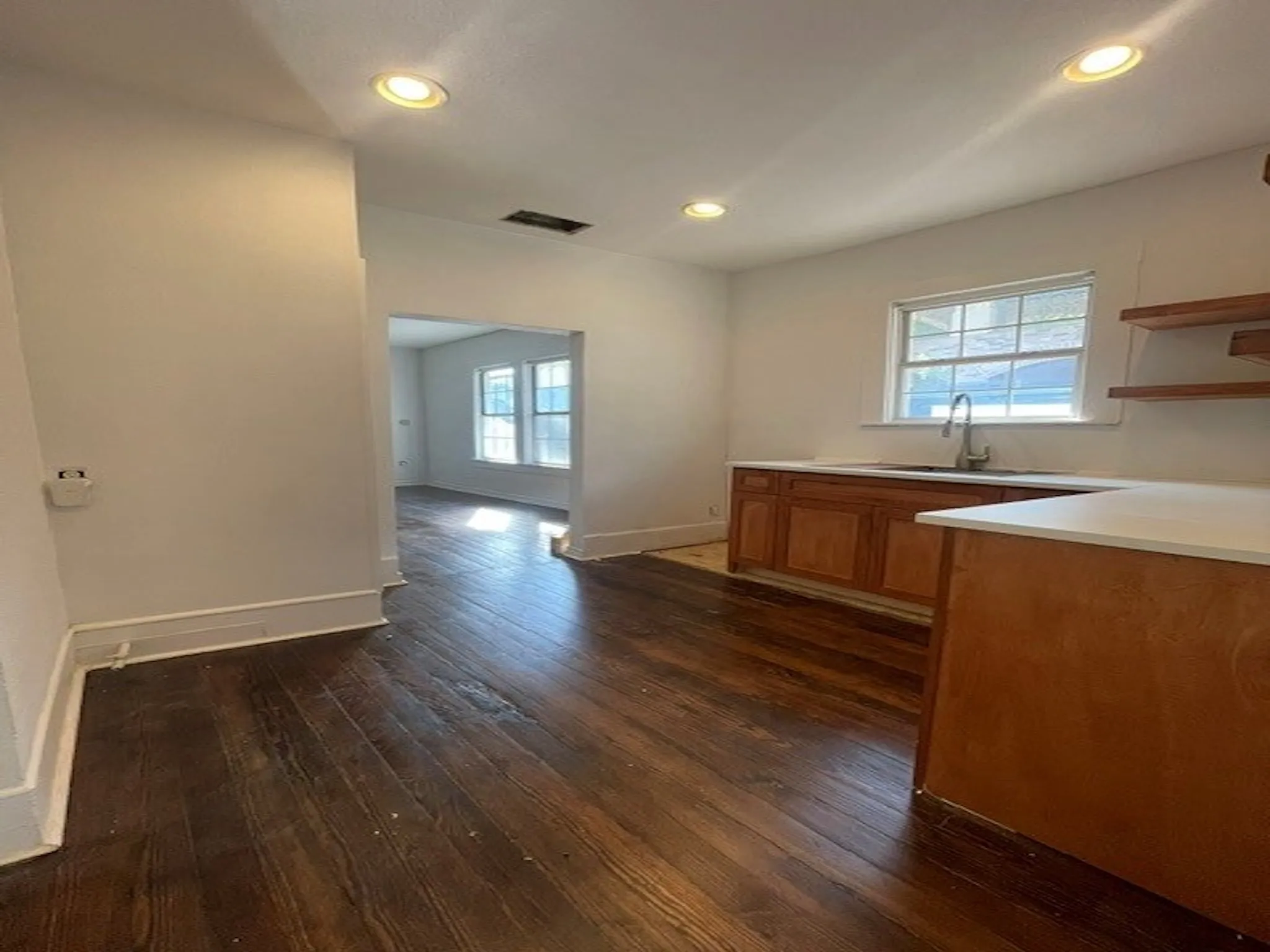 Wood-finish flooring throughout, recessed ceiling lighting, light-toned cabinetry, white countertops, and a stainless steel sink with a pull-down faucet